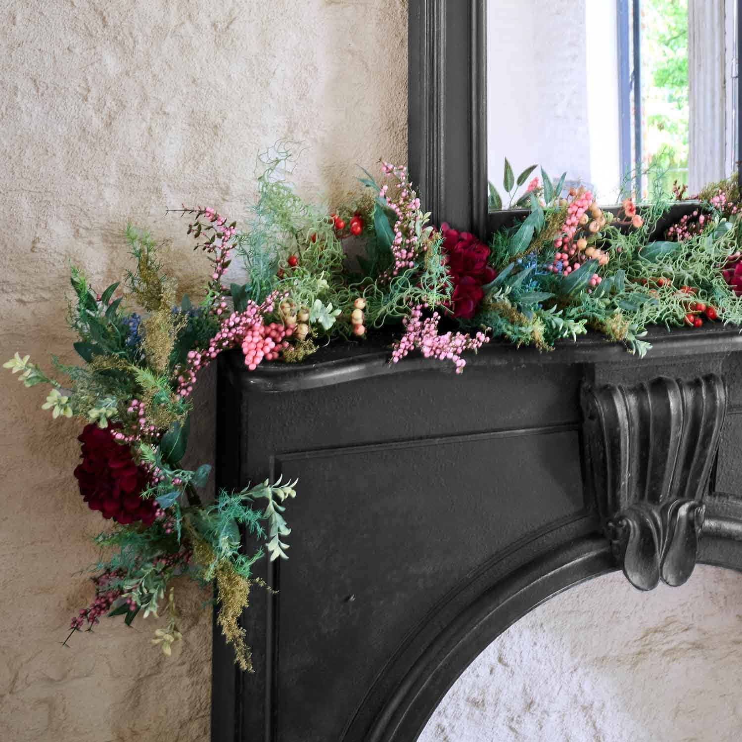 Guirnalda decorativa con bayas rojas y rosas y hojas verdes sobre chimenea negra