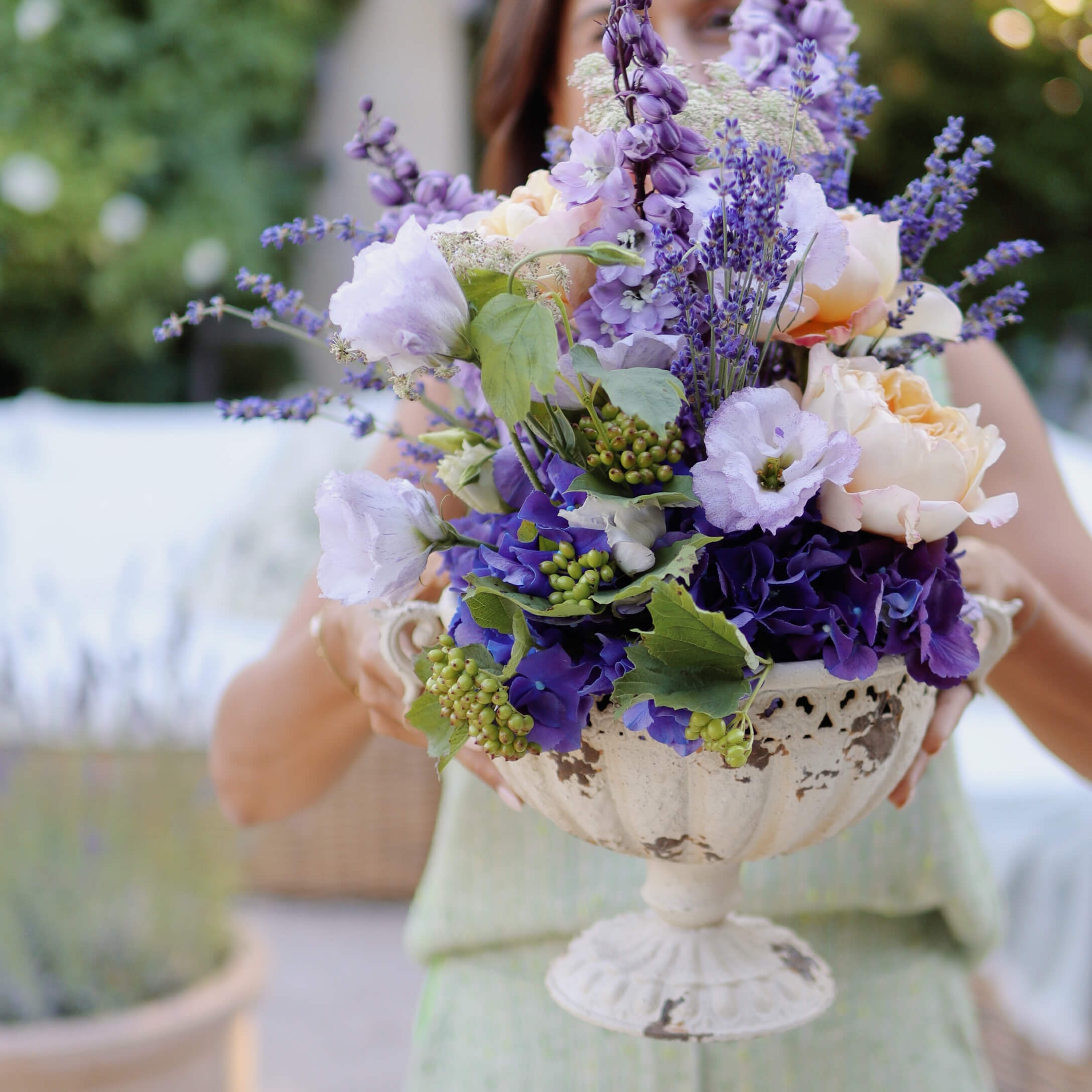 Ramo de flores violetas y crema en jarrón decorativo de cerámica blanca con pie