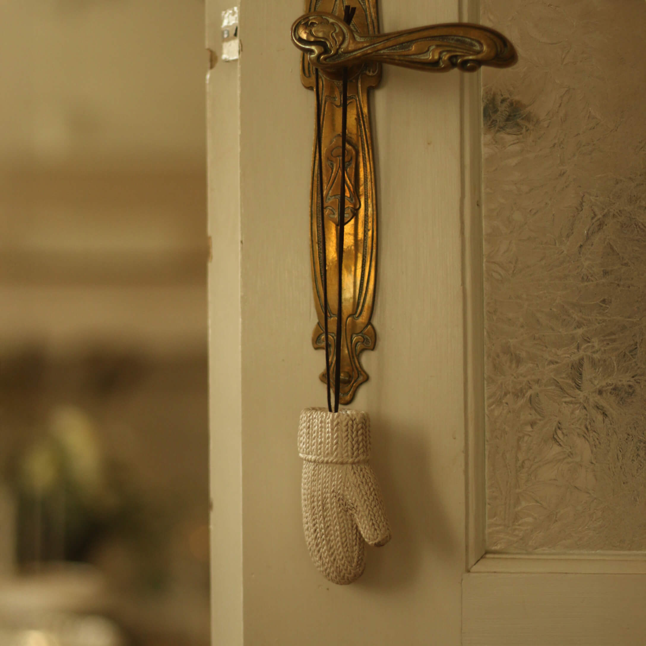 Manopla blanca de punto colgada en un tirador de puerta de latón dorado decorativo