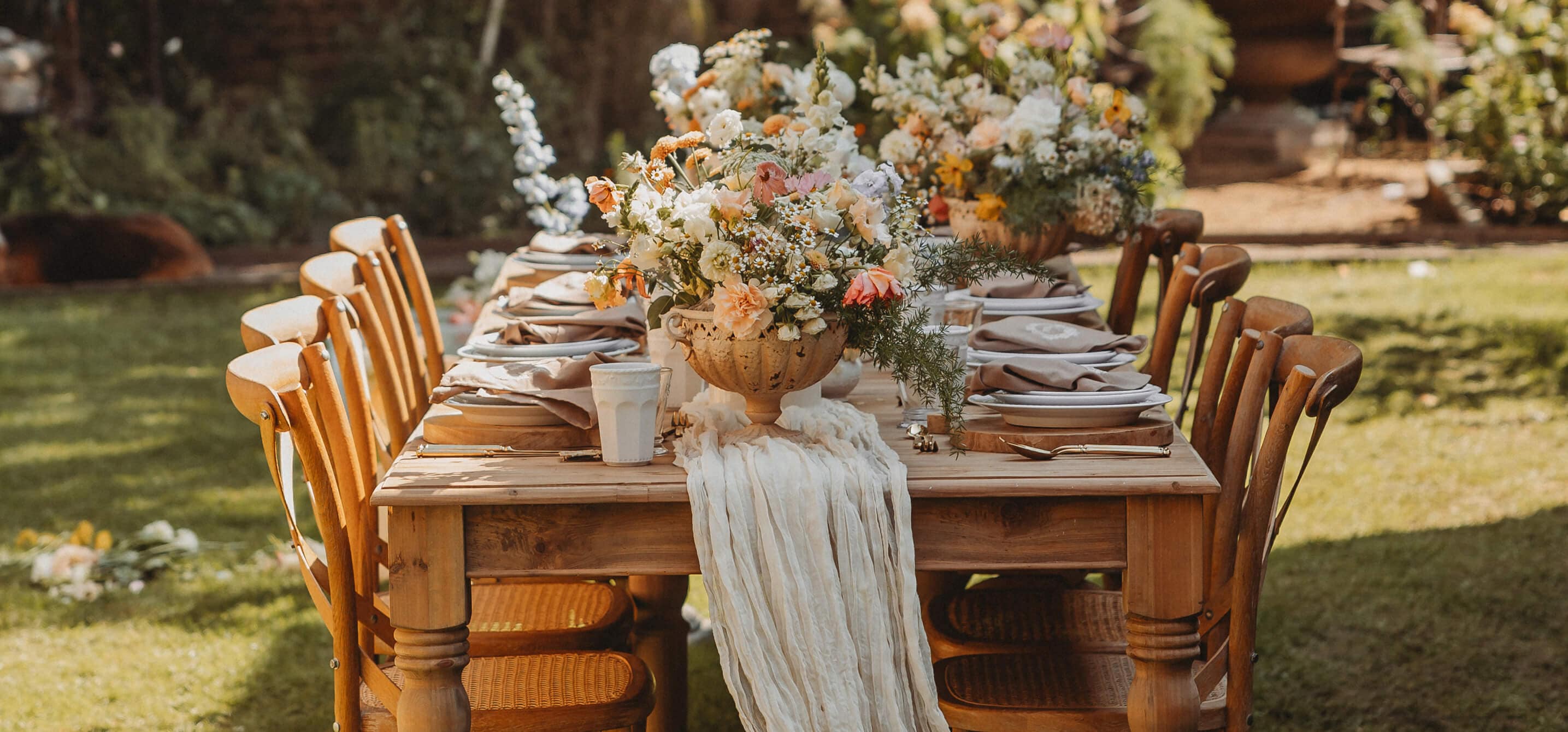 Mesa de jardín de madera con decoración floral y servilletas beige para una reunión veraniega al aire libre