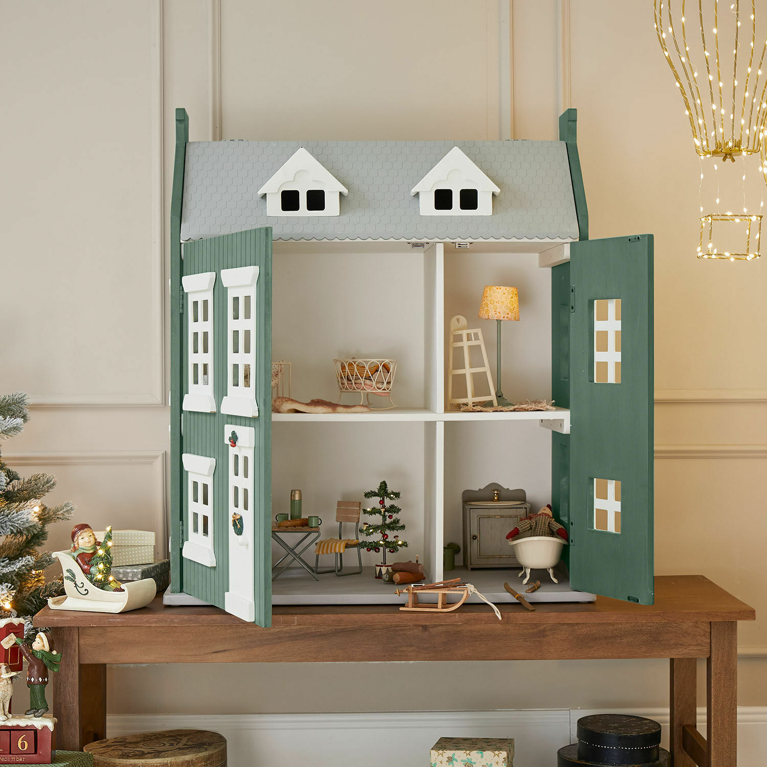 Casa de muñecas Avenari Casa de muñecas de madera verde y blanca con muebles y decoración navideña sobre mesa de madera