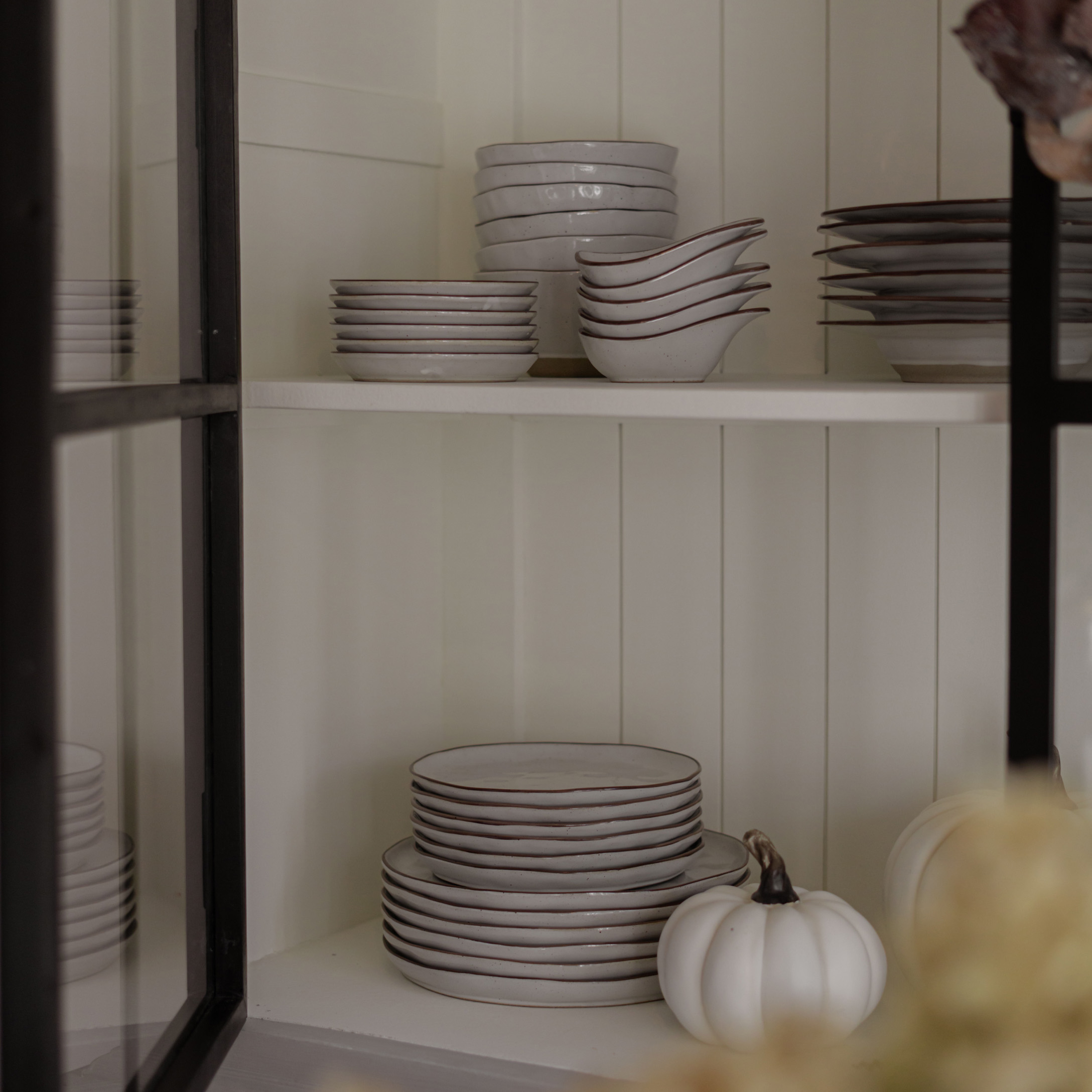 Conjunto de cerámica blanca con borde marrón en estante, calabaza blanca decorativa al lado, estilo rústico