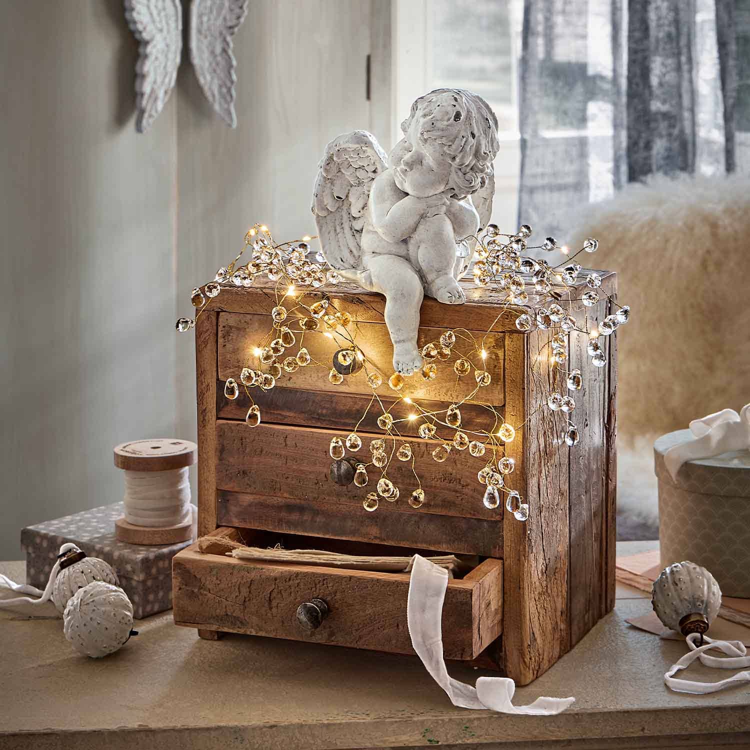Figura de ángel de cerámica blanca sobre caja de madera decorada con luces LED cálidas