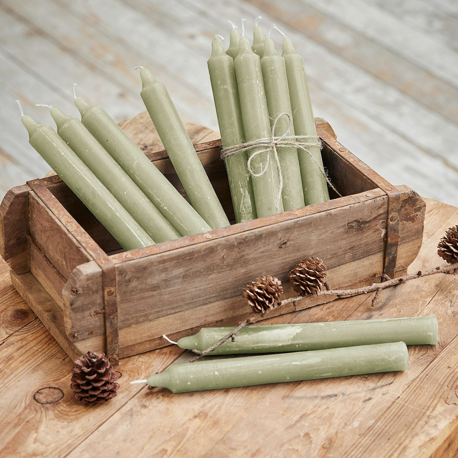 Set de 12 velas Bauceau Conjunto de velas verdes de cera en caja de madera sobre mesa rústica con piñas