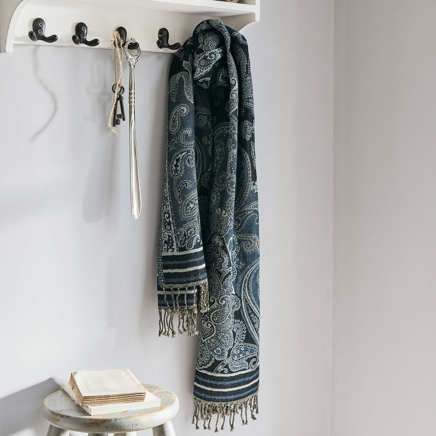 Chal Eloas Bufanda azul marino con diseño paisley y flecos colgada en perchero blanco en interior luminoso