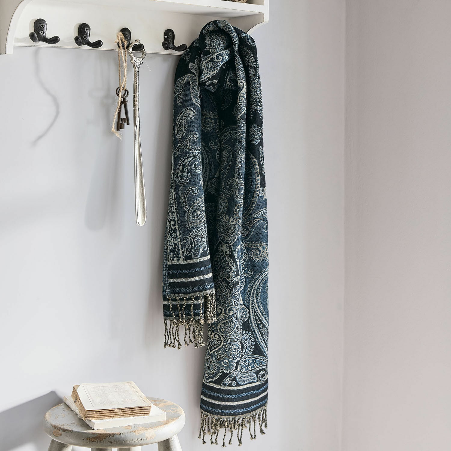 Chal Eloas Bufanda azul marino con diseño paisley y flecos colgada en perchero blanco en interior luminoso