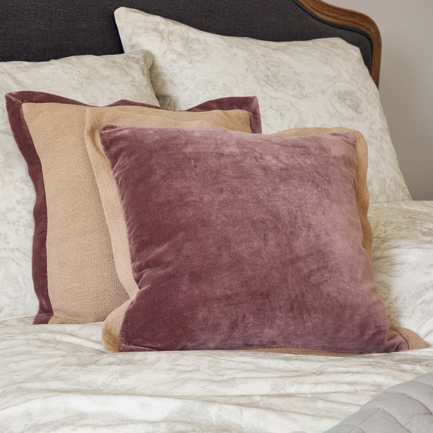 Conjunto de cojines decorativos de terciopelo y lino en rosa y beige sobre cama con estampado floral