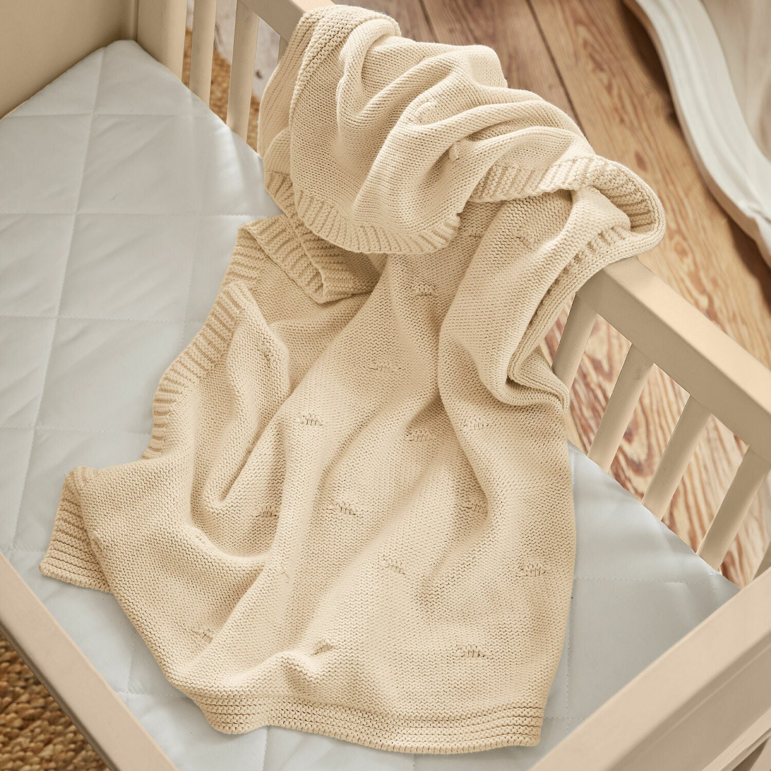 Plaid Samiya Manta beige de algodón tejido sobre cuna de madera clara, suave y acogedora