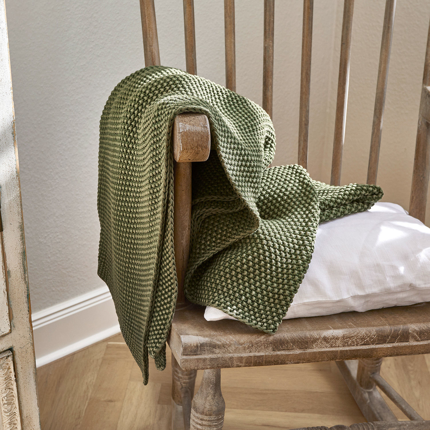 Plaid Amberley Manta verde de algodón tejido sobre silla de madera con cojín blanco, decoración acogedora