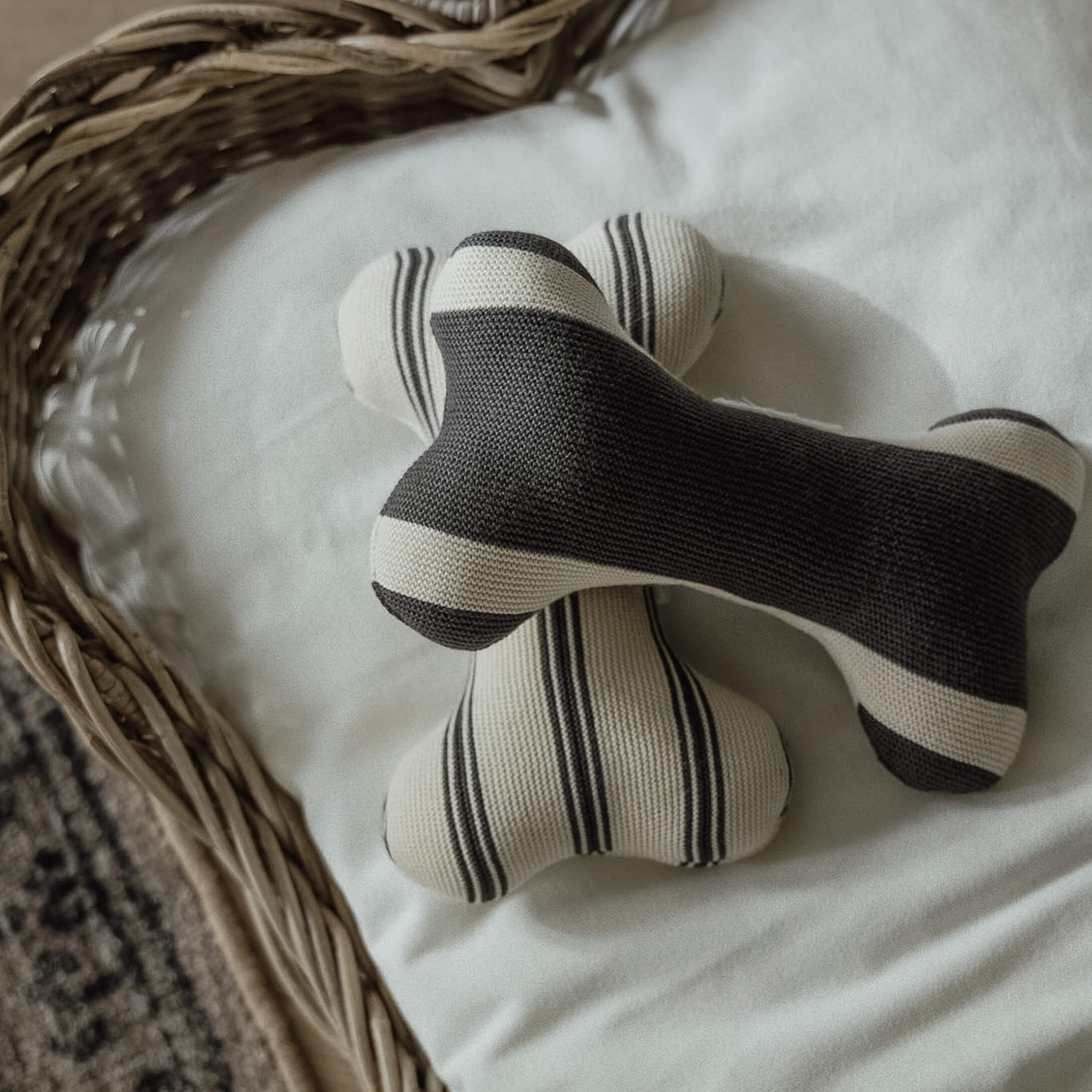 Dos juguetes tejidos en forma de hueso con rayas blancas y negras sobre fondo blanco en cesta de mimbre