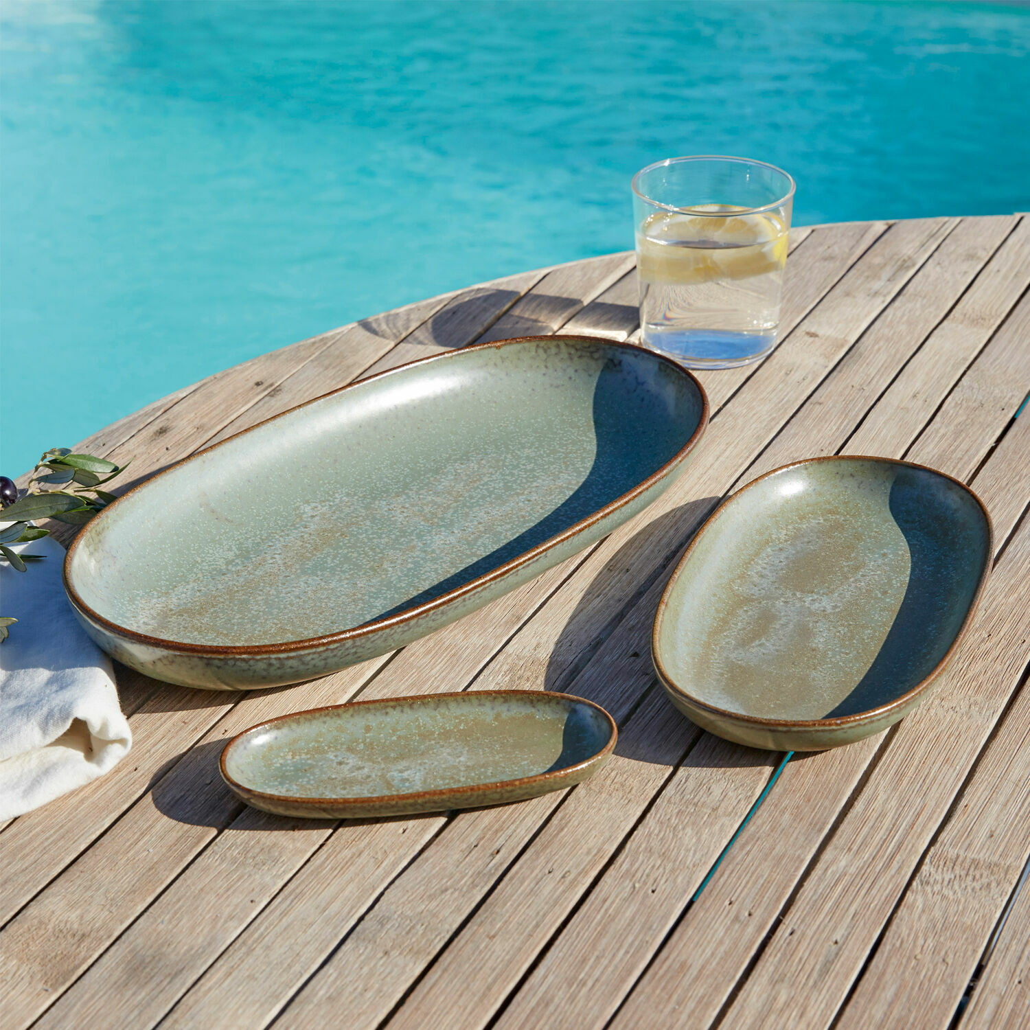 Set de 3 platos Biarré Conjunto de tres platos de cerámica verde sobre mesa de madera junto a piscina