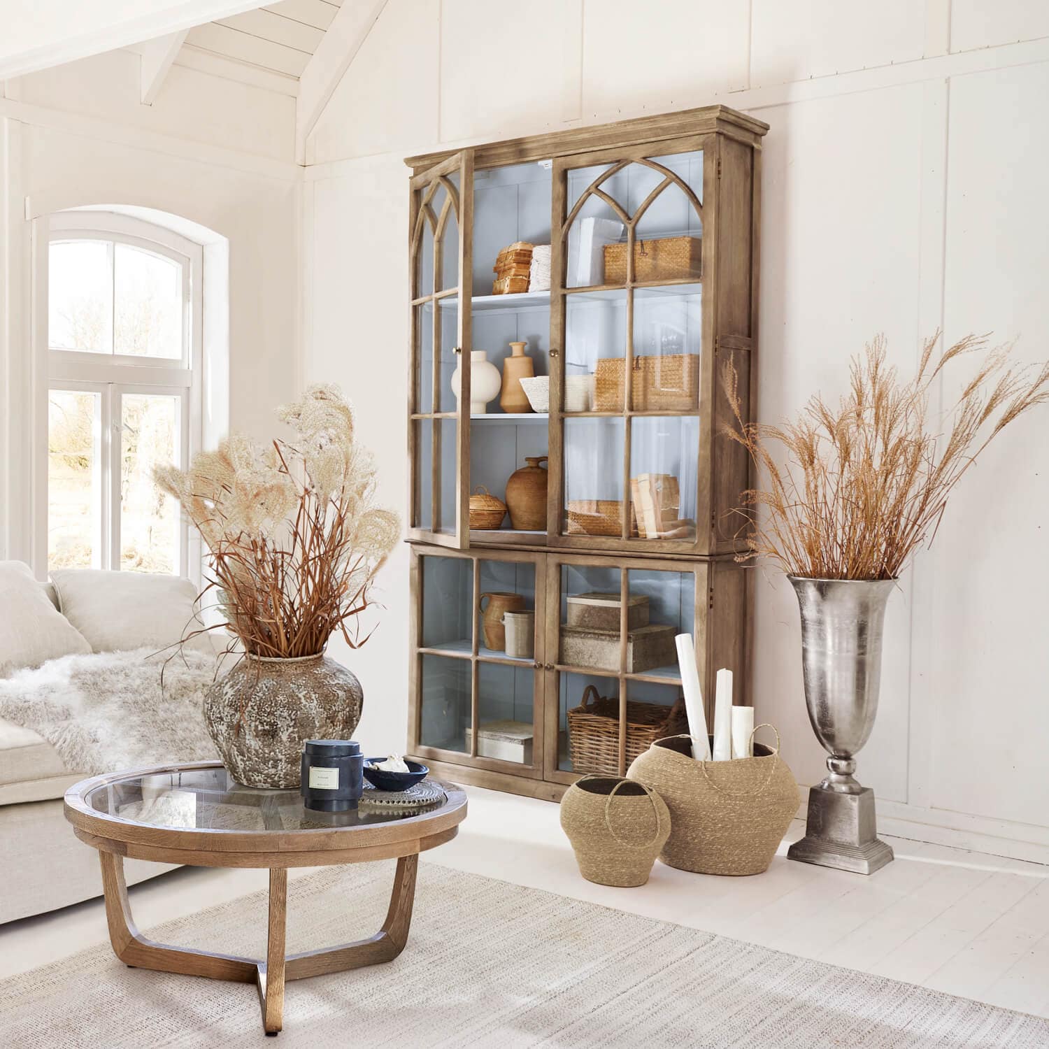 Salón acogedor con vitrina de madera, mesa de cristal y decoraciones naturales en tonos claros