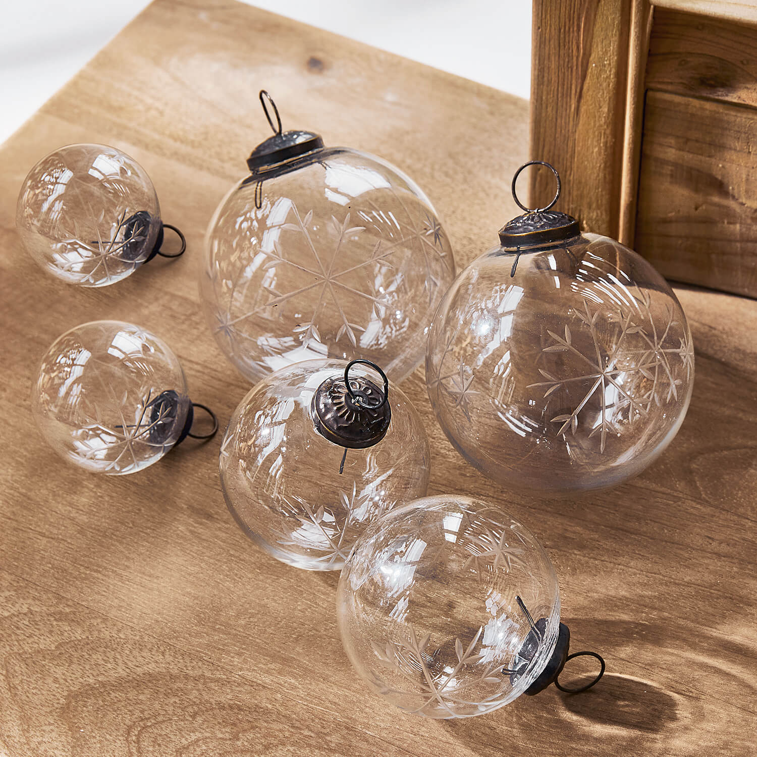 Bolas de Navidad de vidrio transparente con diseño grabado de copos de nieve sobre mesa de madera, decoración