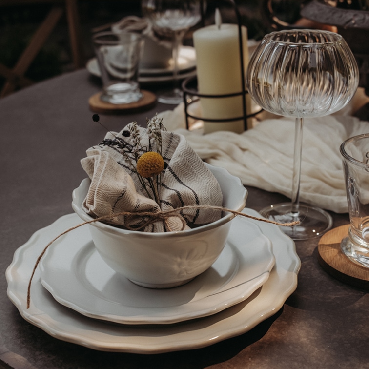 Conjunto de vajilla de cerámica blanca con cuenco, platos y servilleta de lino decorada con flores sobre mesa