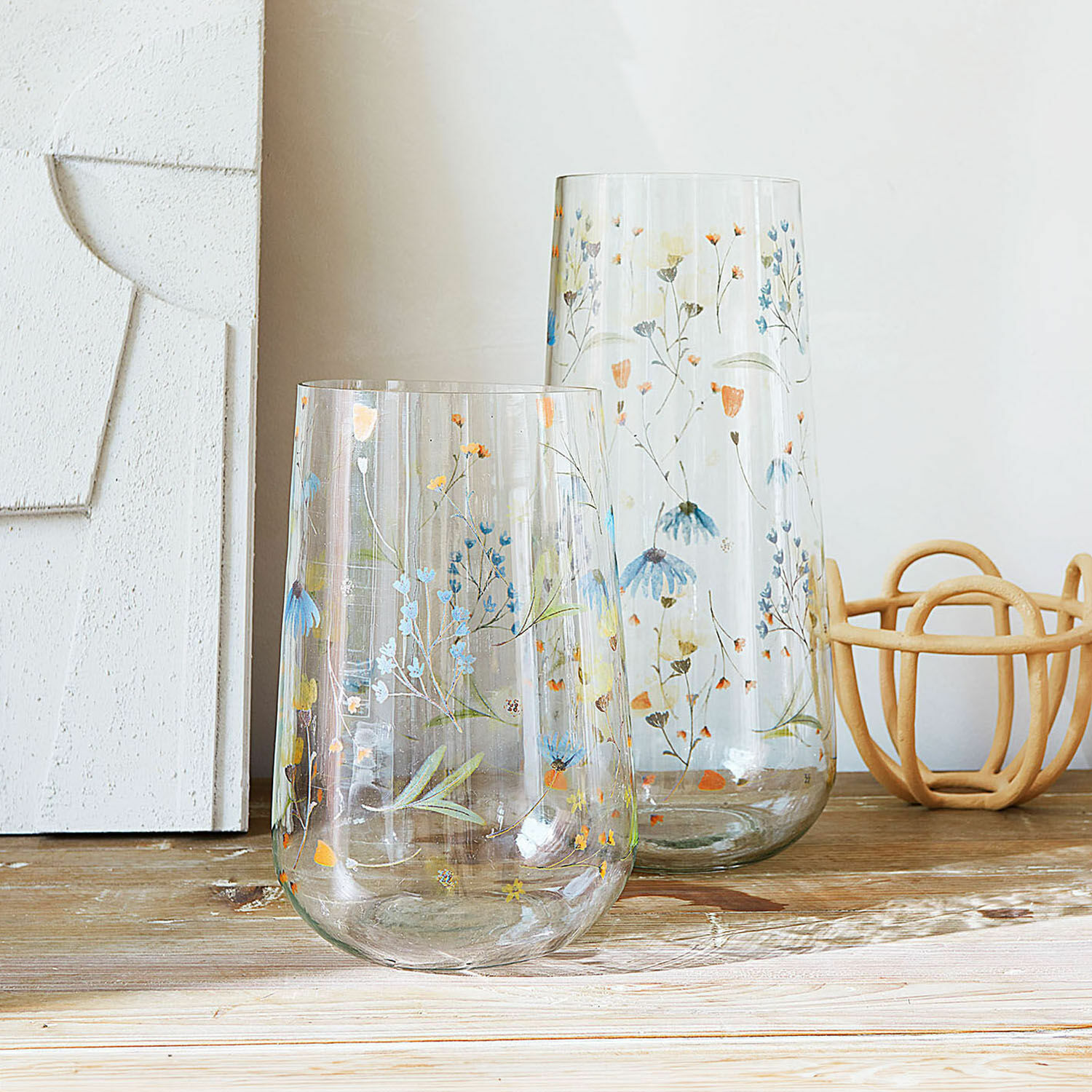 Set de 2 jarrones Nervila Dos jarrones de vidrio transparente con diseño floral colorido sobre mesa de madera