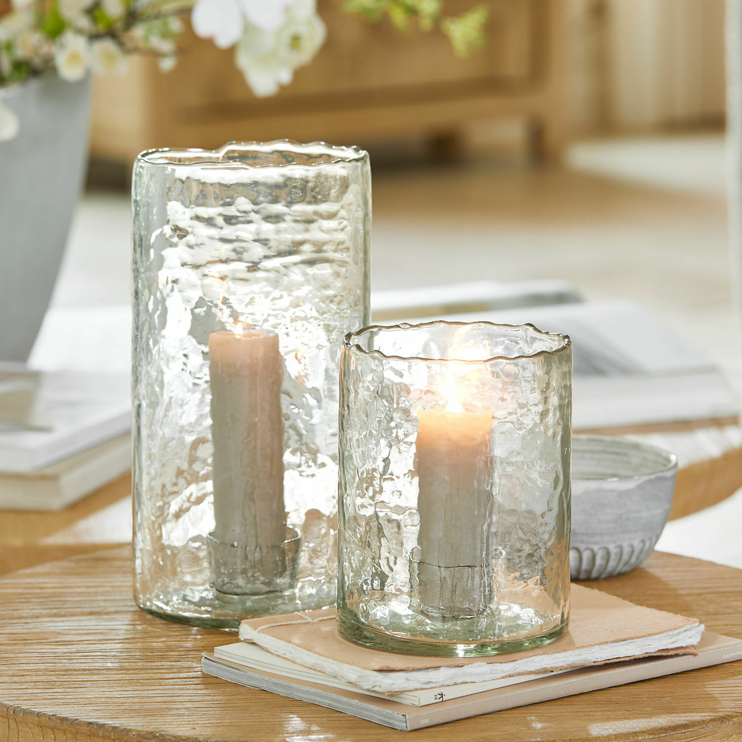 Set de 2 portavelas Querlay Portavelas de vidrio transparente texturizado con velas blancas sobre mesa de madera clara