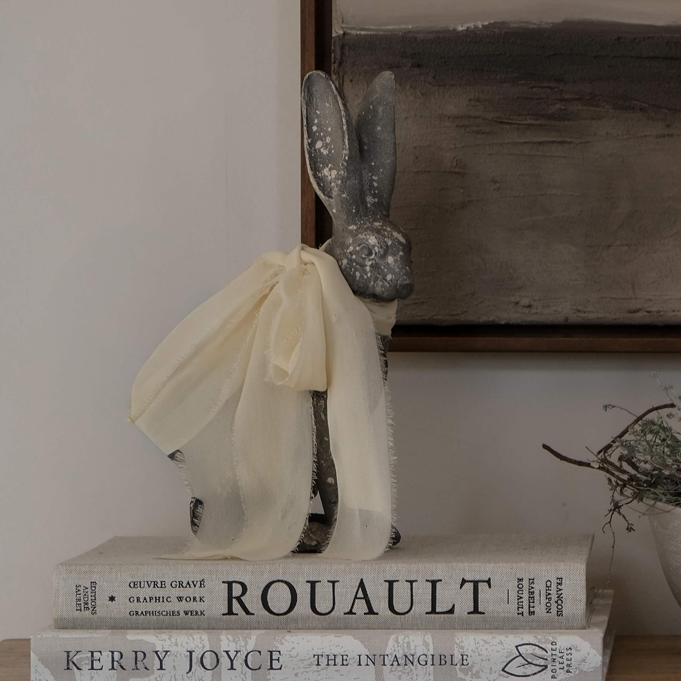 Conejo decorativo gris con lazo de tela crema sobre una pila de libros vintage