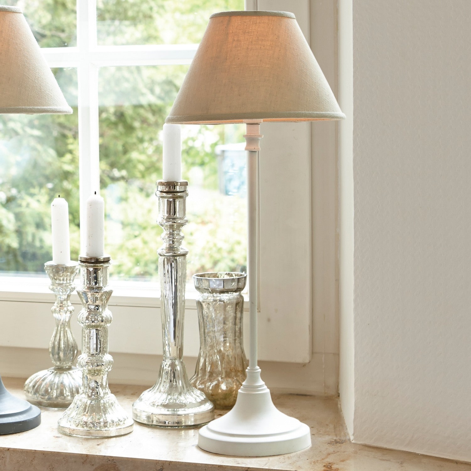 Lámpara de mesa blanca de metal con pantalla beige sobre alféizar con candelabros decorativos