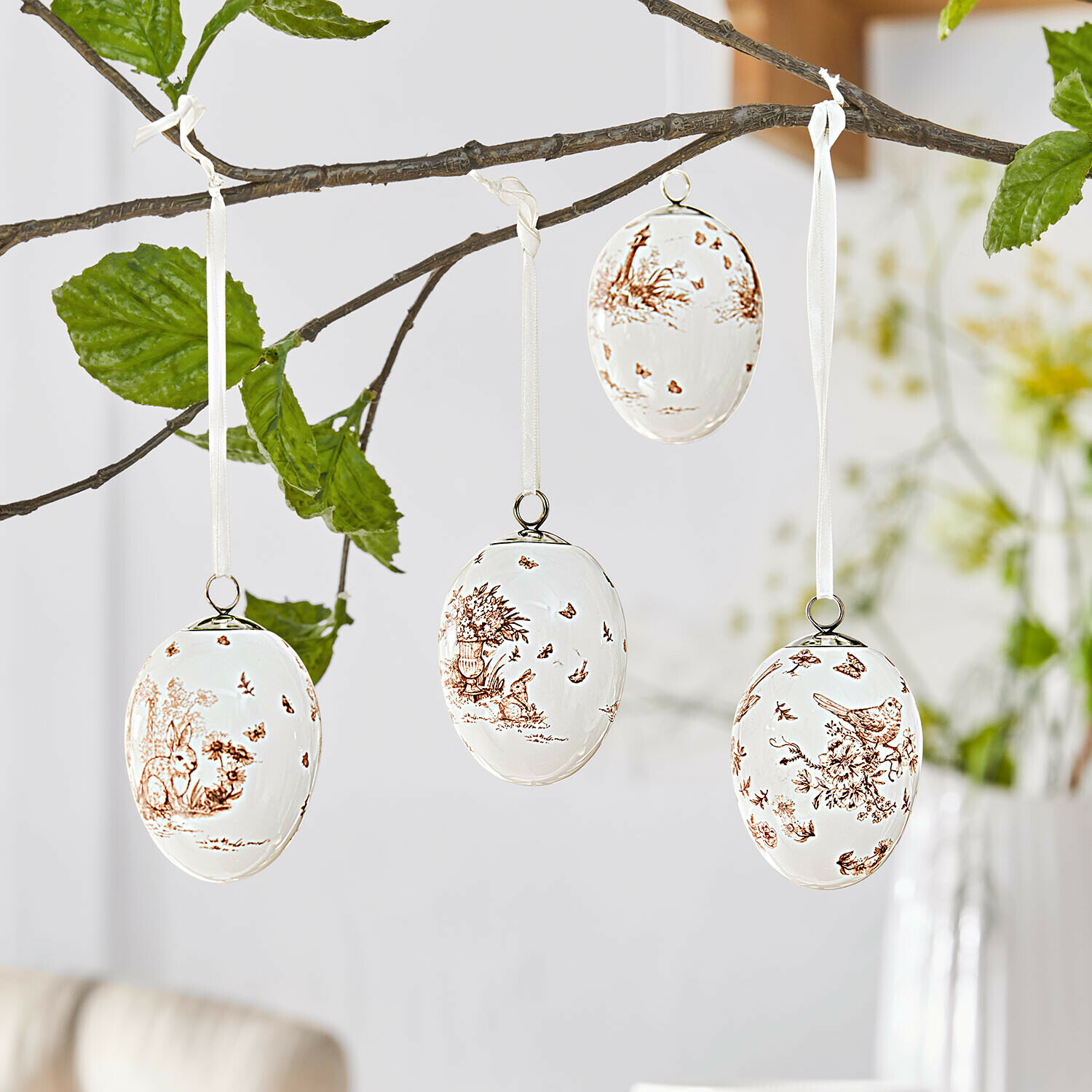 Set de 4 colgantes Seravoux Huevos de Pascua de cerámica blanca con motivos marrones de animales y plantas colgados de una rama