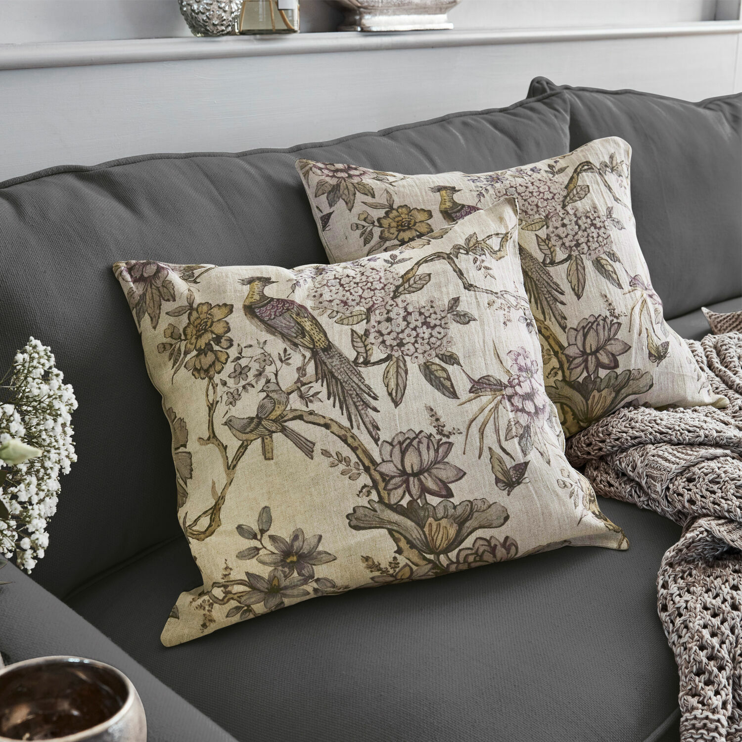 Cojines decorativos de lino con estampado de pájaros y flores sobre sofá gris, accesorios elegantes para salón