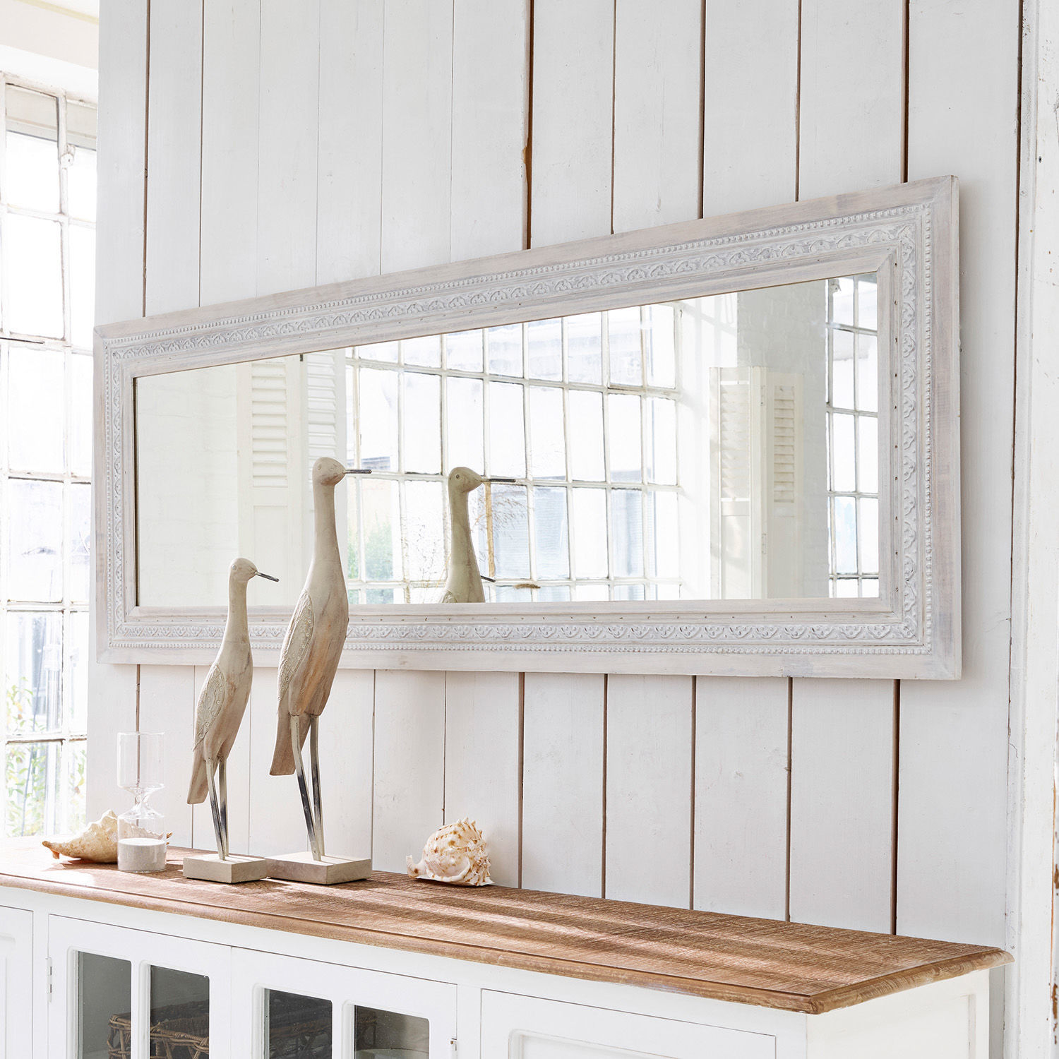 Espejo Milanu Gran espejo rectangular con marco de madera blanca sobre aparador blanco con decoraciones de madera y conchas