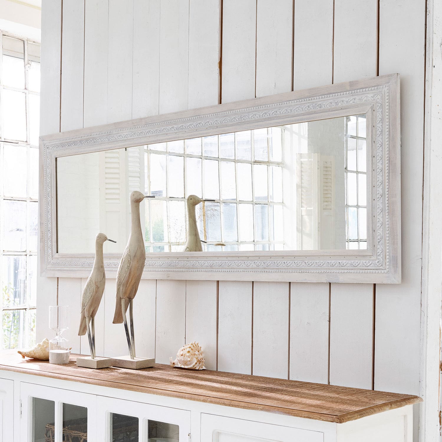 Espejo Milanu Gran espejo rectangular con marco de madera blanca sobre aparador blanco con decoraciones de madera y conchas