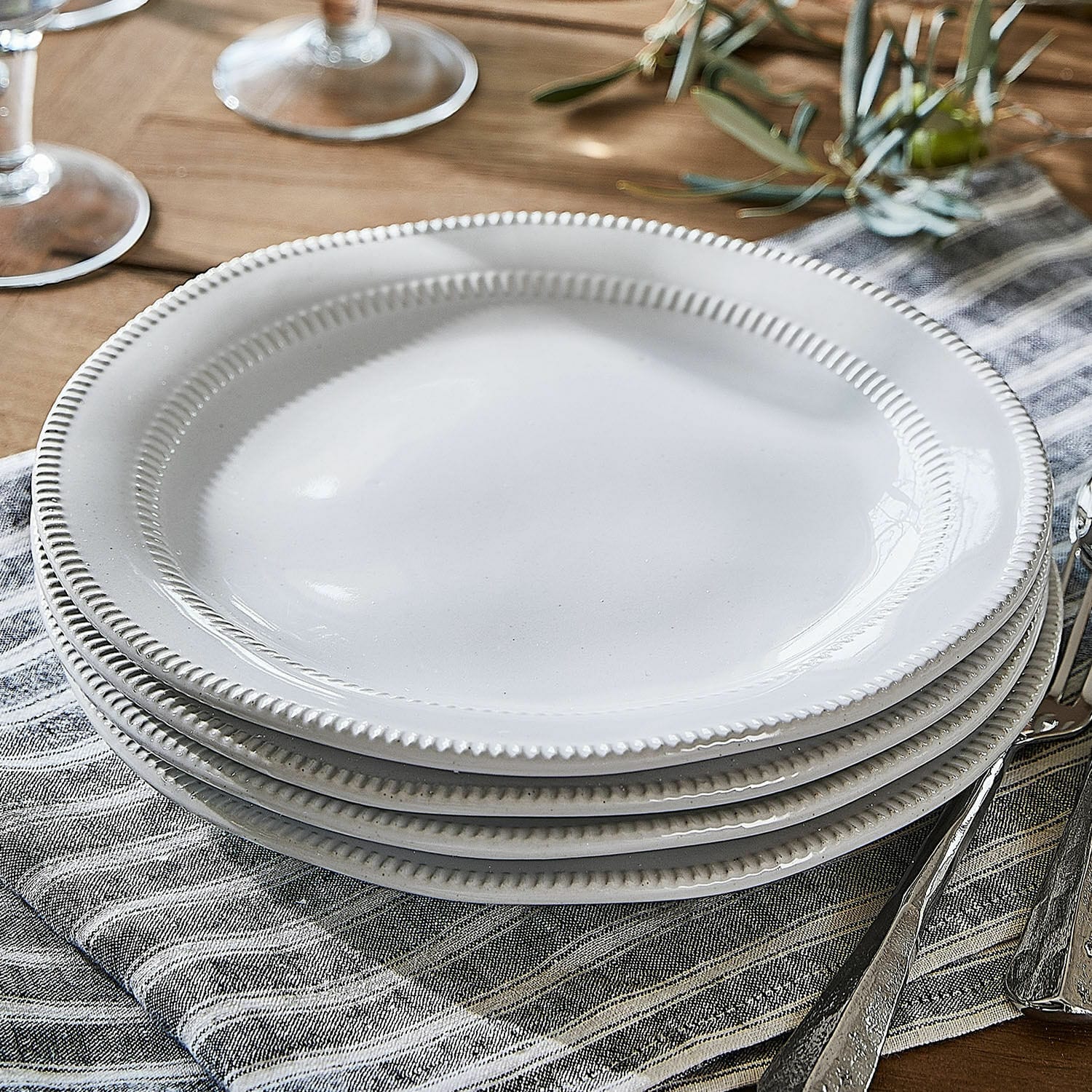 Set de 4 platos de postre Alentejo Platos blancos de cerámica con borde decorativo sobre servilleta de lino en mesa de madera