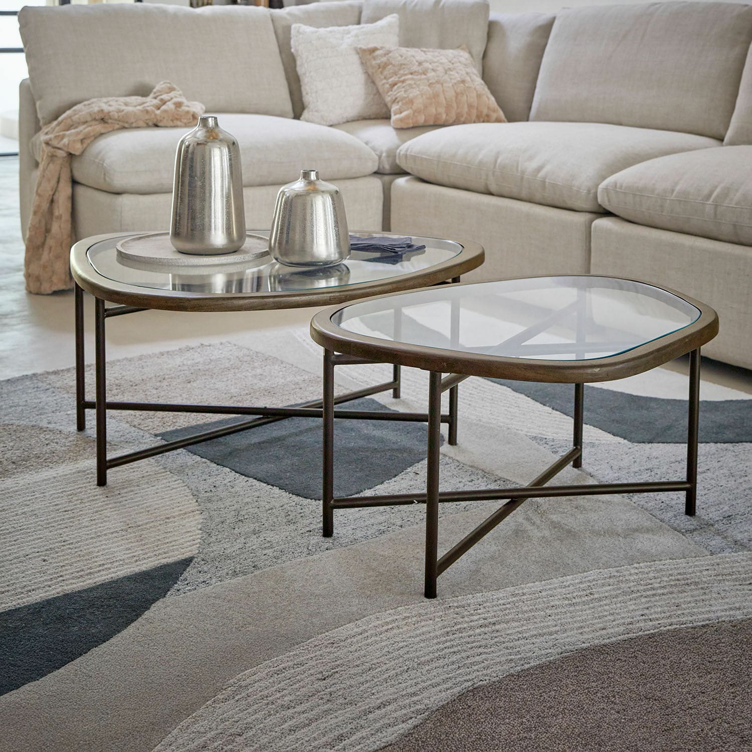Set de 2 mesas de centro Kembria Conjunto de dos mesas de centro con estructura metálica y tapa de cristal en salón con sofá beige