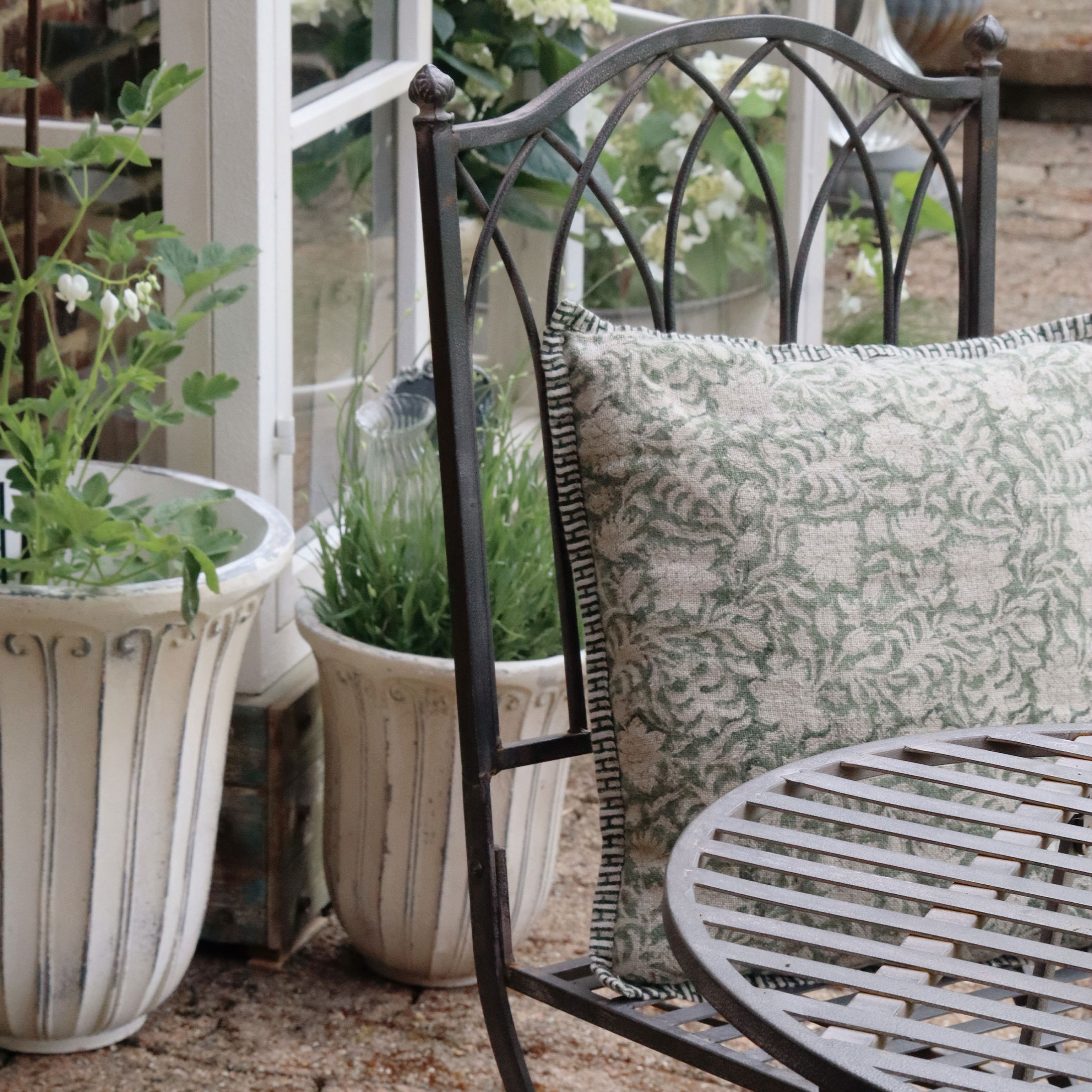 Sillón de jardín de metal con cojín verde y beige, rodeado de macetas decorativas con plantas