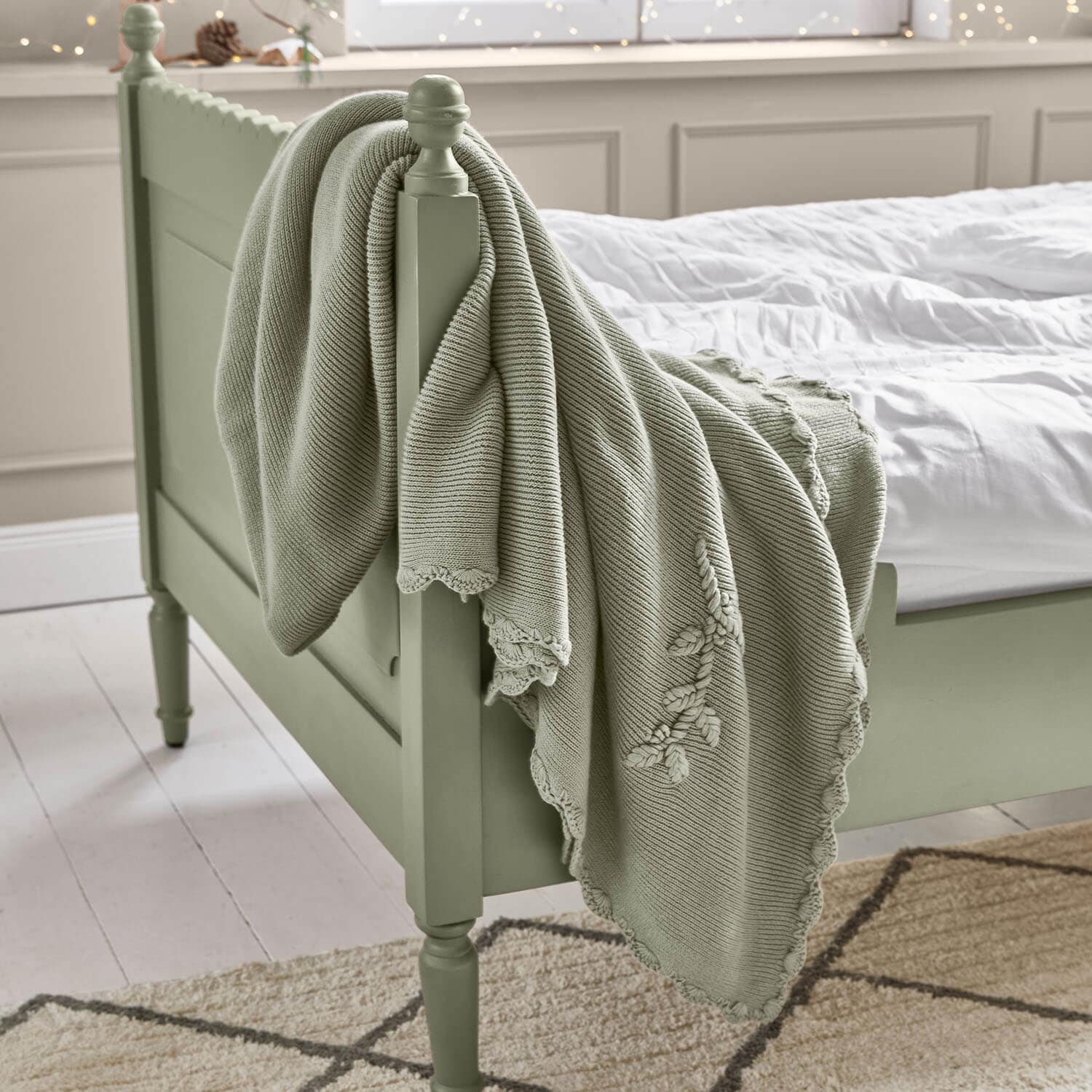 Manta de algodón verde menta con bordado decorativo sobre cama de madera en dormitorio