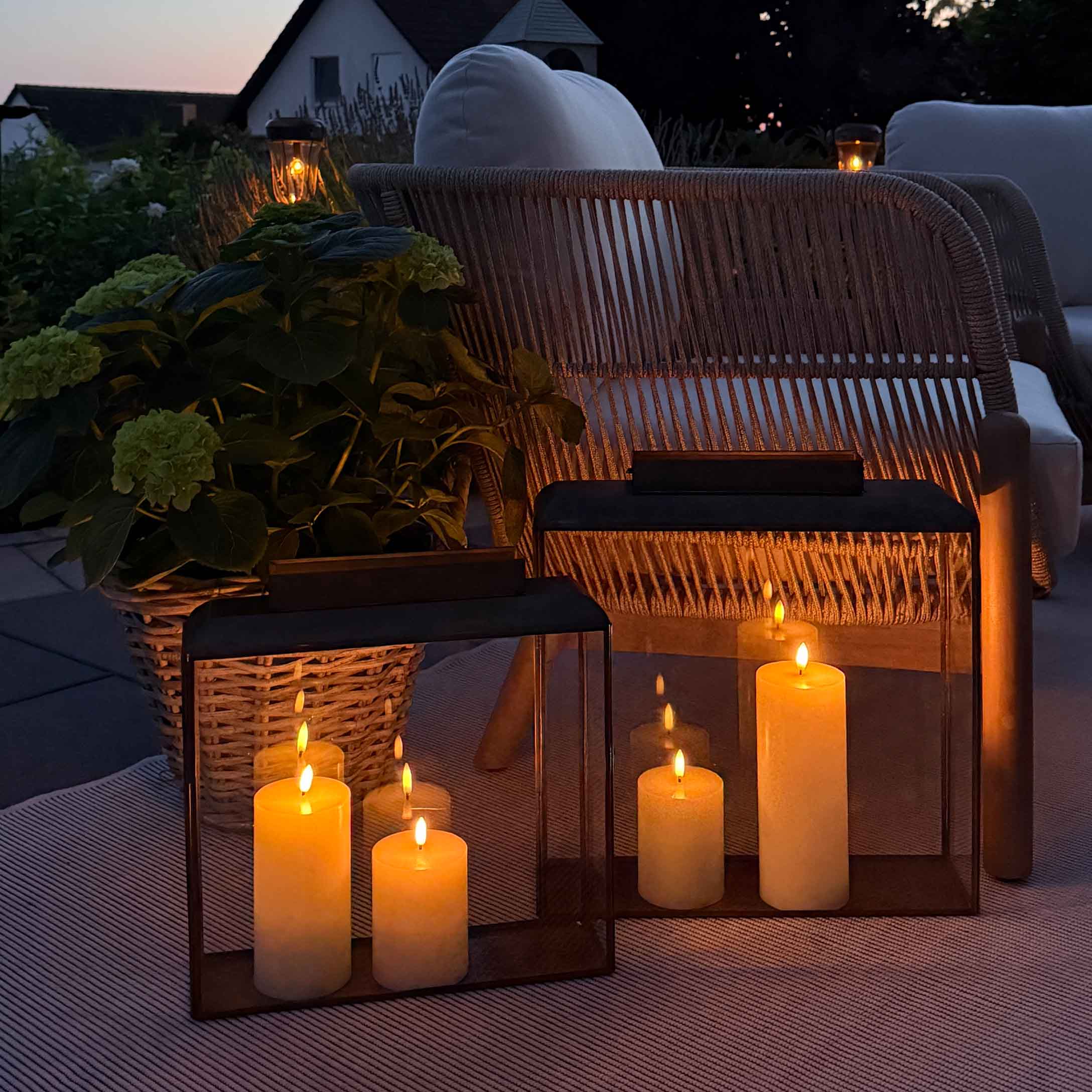 Iluminación ambiental con faroles y velas en terraza con sillón de mimbre y cojín blanco