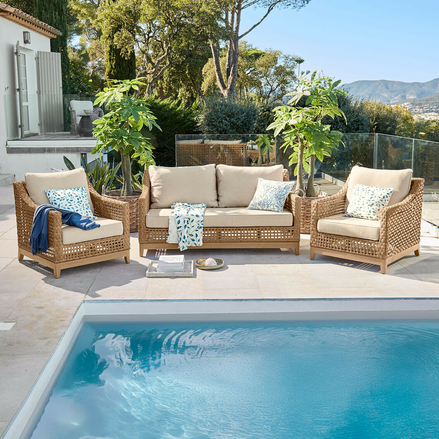 Conjunto de muebles de jardín de ratán marrón con cojines beige junto a una piscina