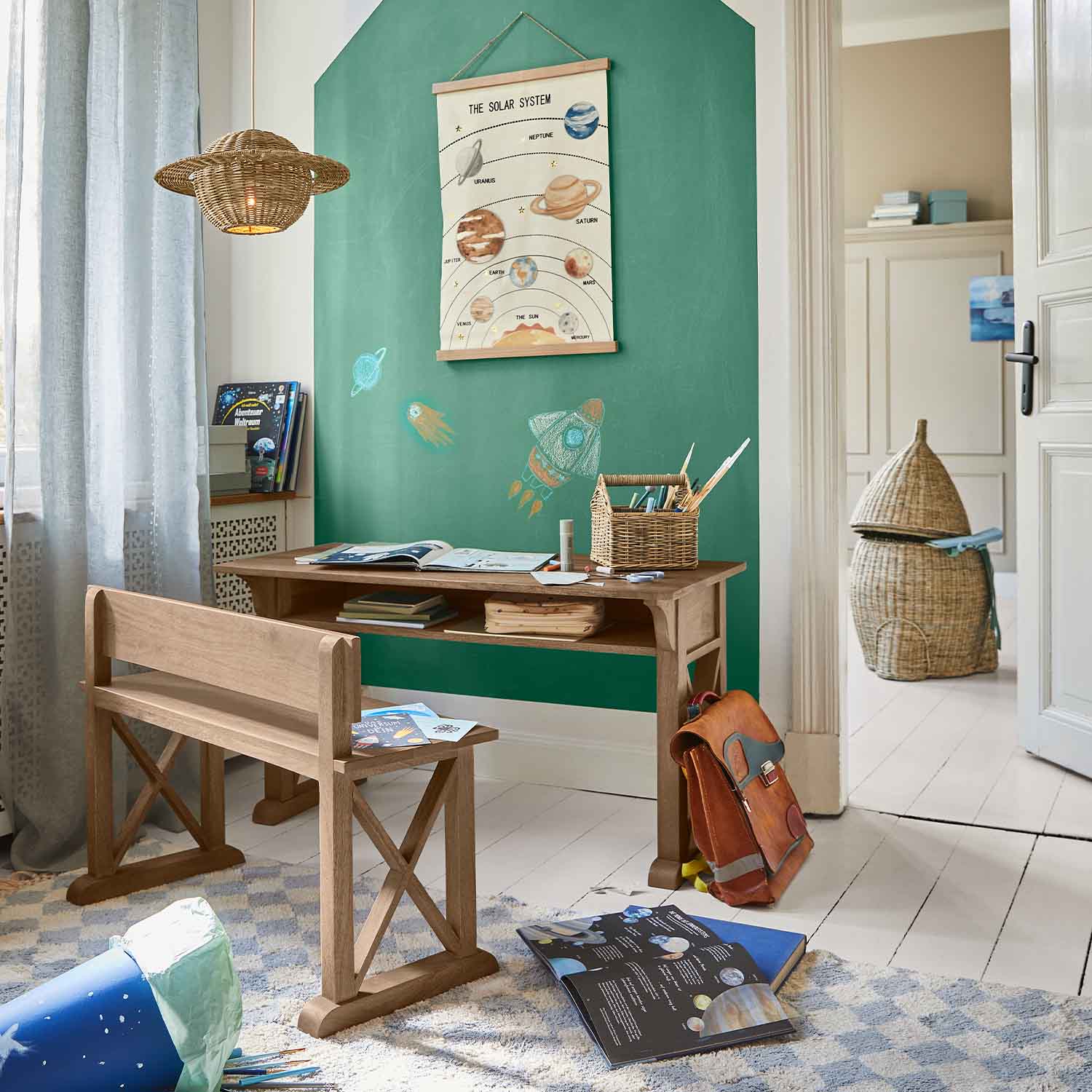 Escritorio y banco de madera en habitación infantil con pared verde y póster del sistema solar