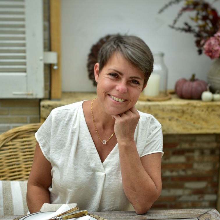 Mujer sonriente con blusa blanca sentada en mesa con decoración otoñal de fondo