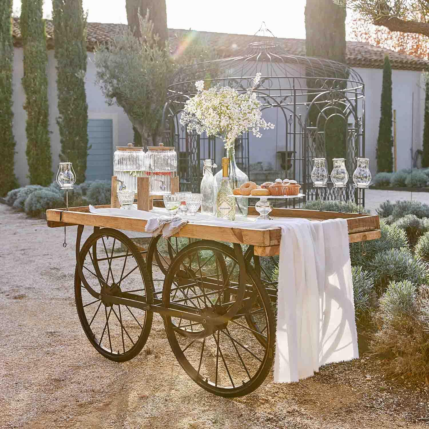 Carro de madera con ruedas de metal decorado con jarras de cristal y flores en un jardín soleado