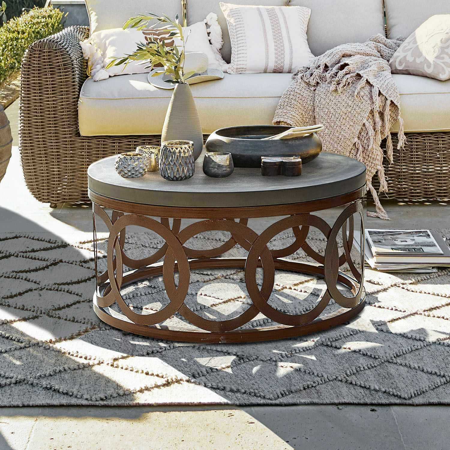 Mesa de centro Boécourt Mesa de centro redonda con base metálica oxidada y superficie gris en terraza con sofá de mimbre beige
