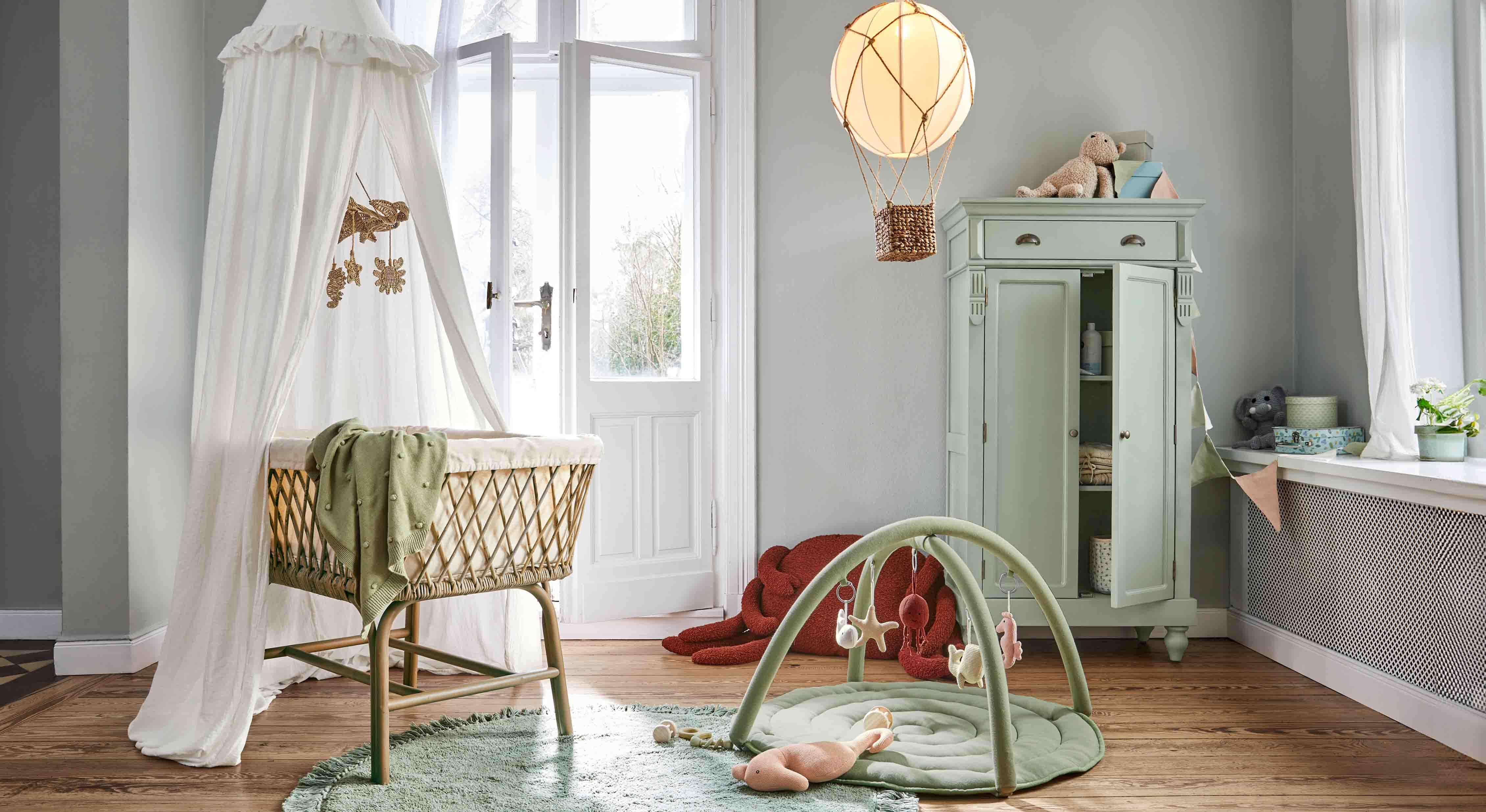 Acogedora habitación infantil con cuna de mimbre, alfombra verde y armario pastel para juguetes y almacenamiento