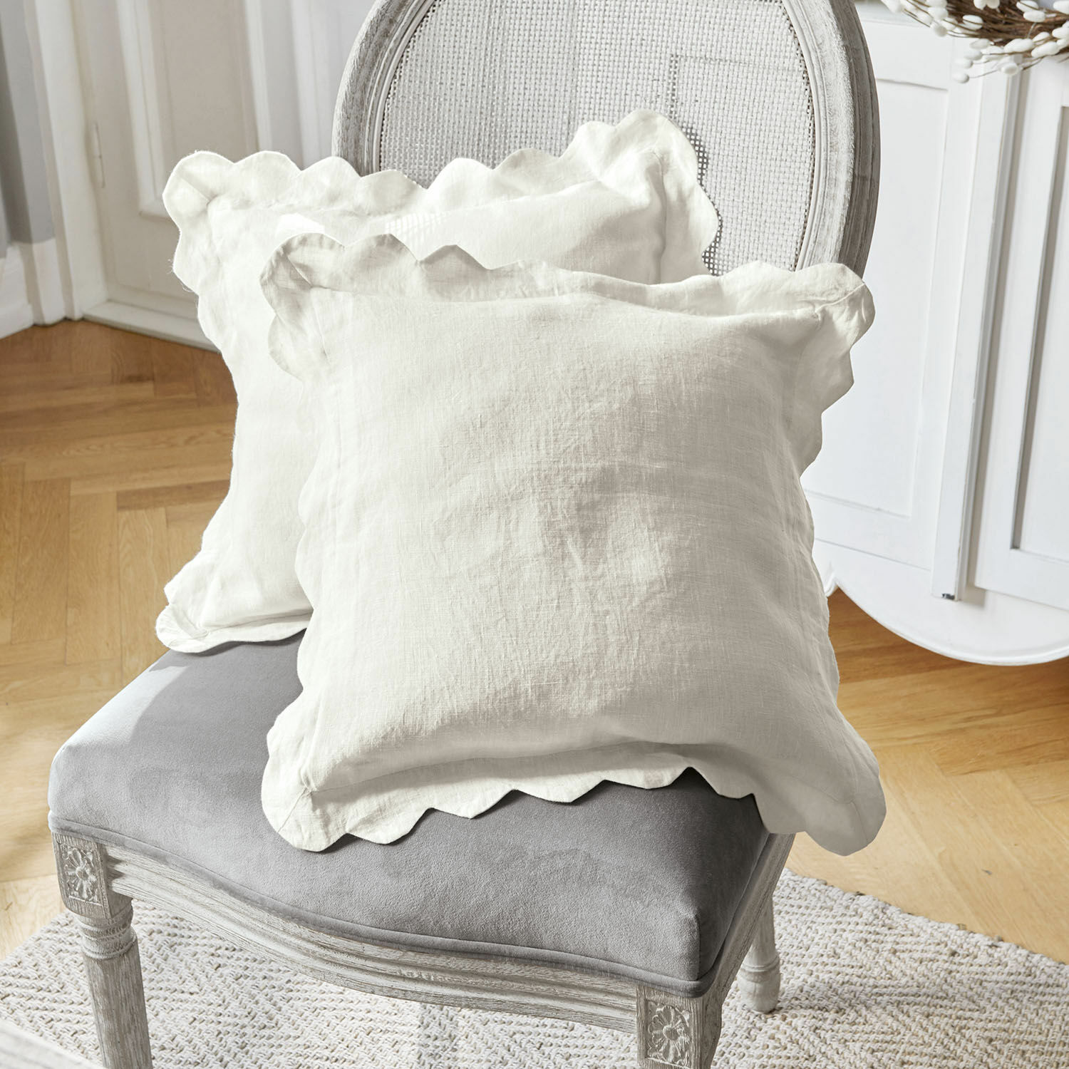 Set de 2 fundas de cojín Fontienne Cojines decorativos de lino blanco con borde ondulado sobre silla tapizada gris en sala