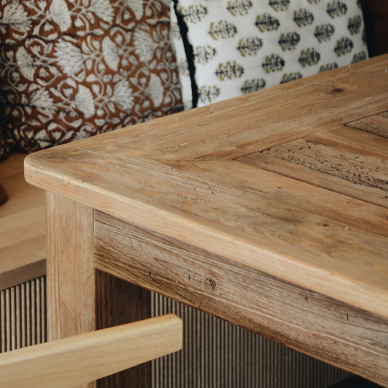 Mesa de madera clara con diseño rústico y cojines decorativos al fondo, muebles de salón