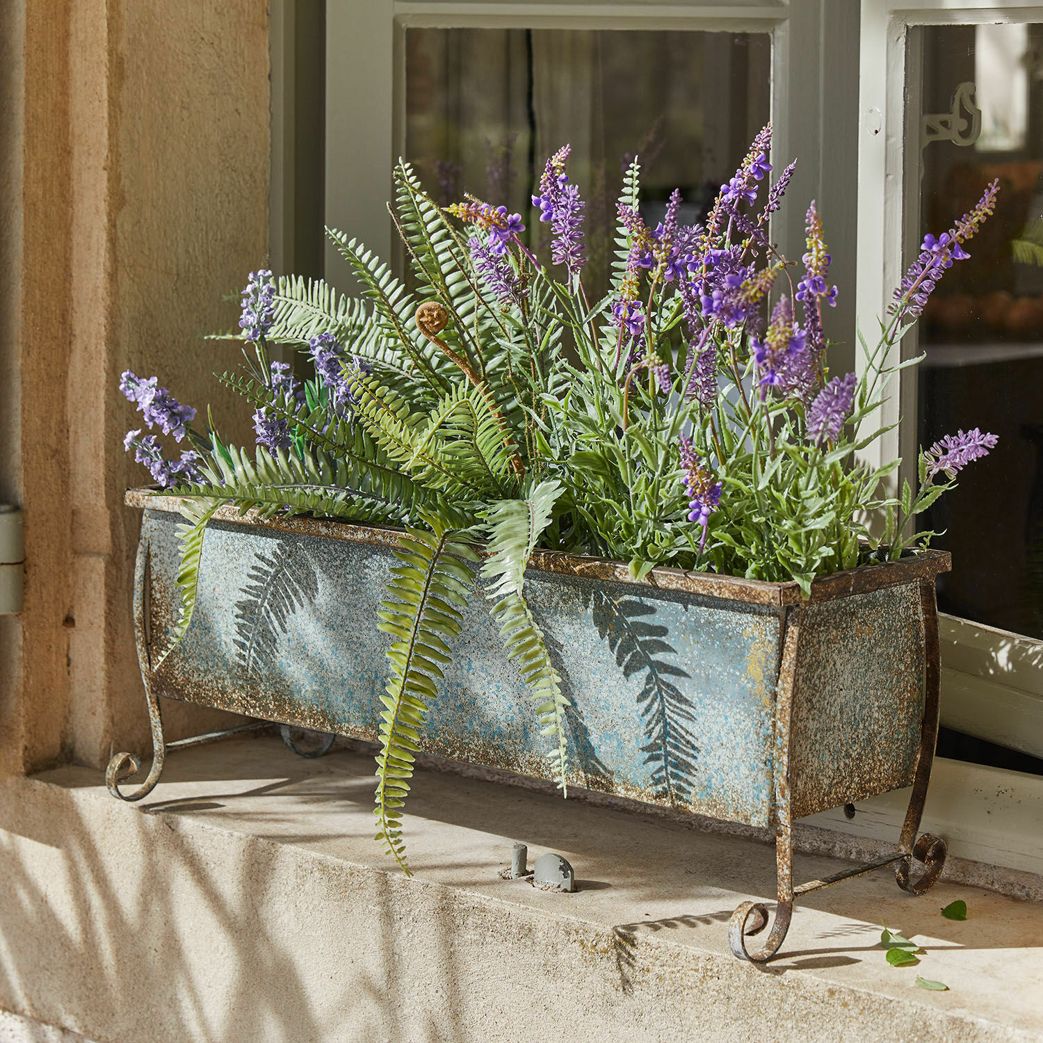 Jardinera metálica vintage con helechos verdes y flores moradas en alféizar de ventana
