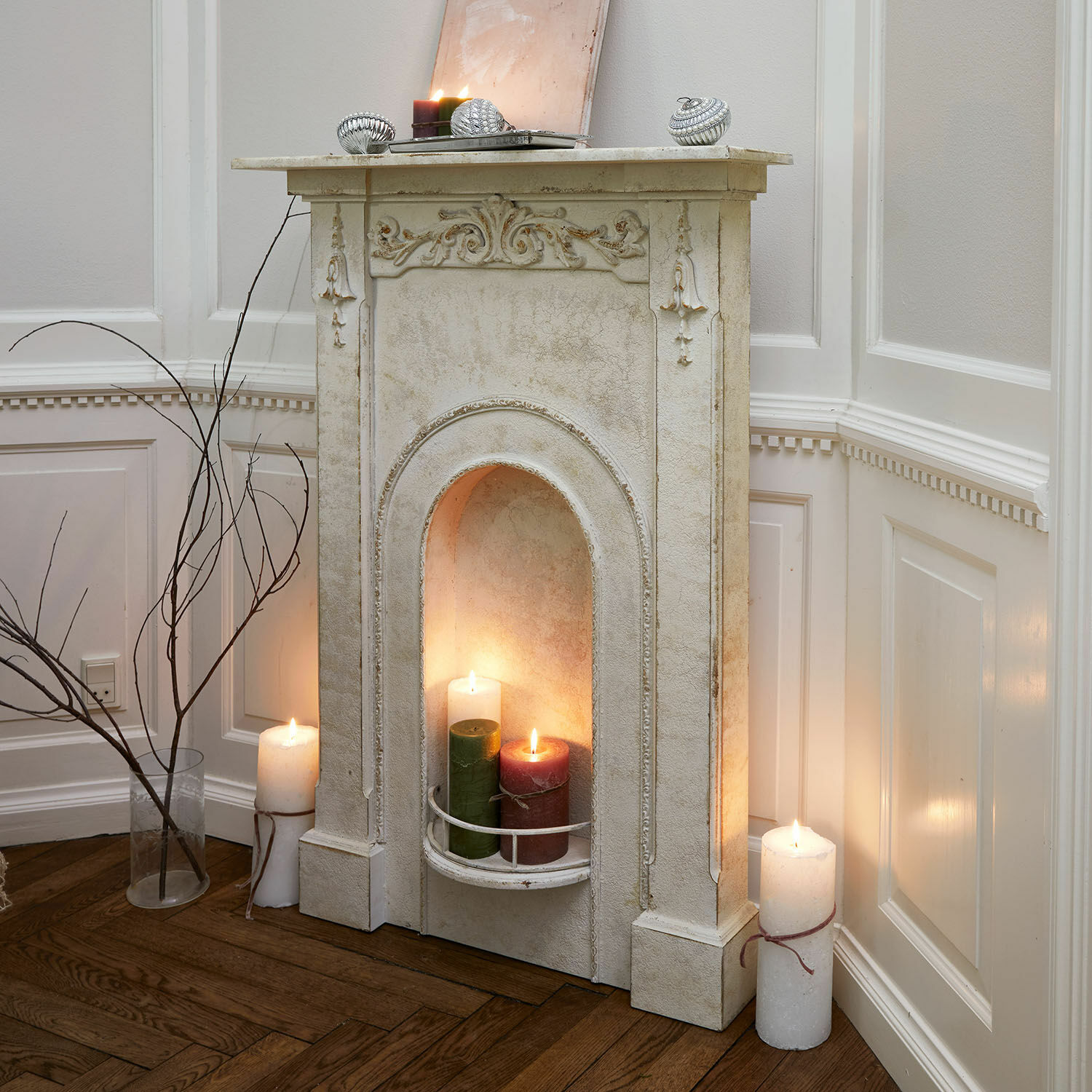 Consola de chimenea Câlanette Chimenea decorativa blanca con detalles ornamentales y velas encendidas en salón con suelo de madera