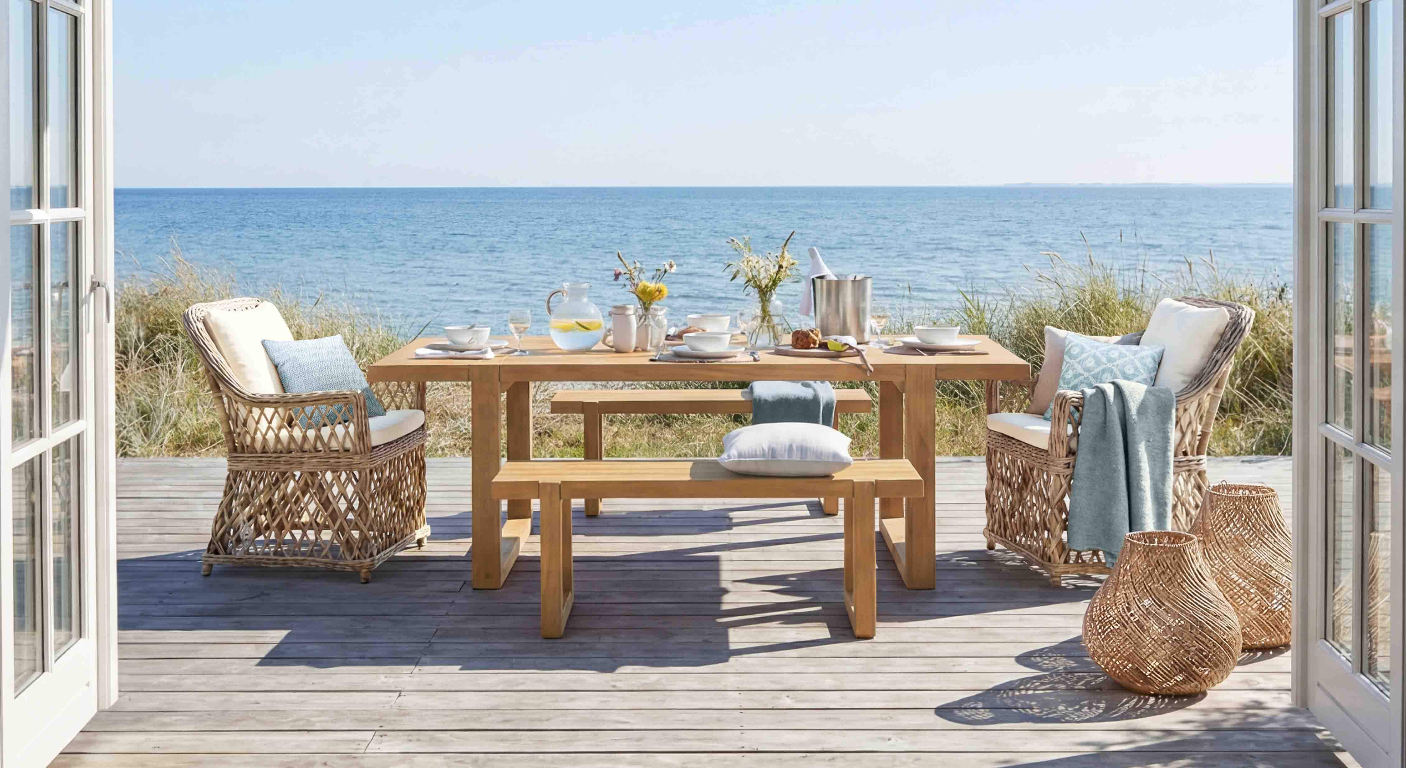 Conjunto de muebles de jardín de madera y ratán en tonos naturales en terraza con vista al mar