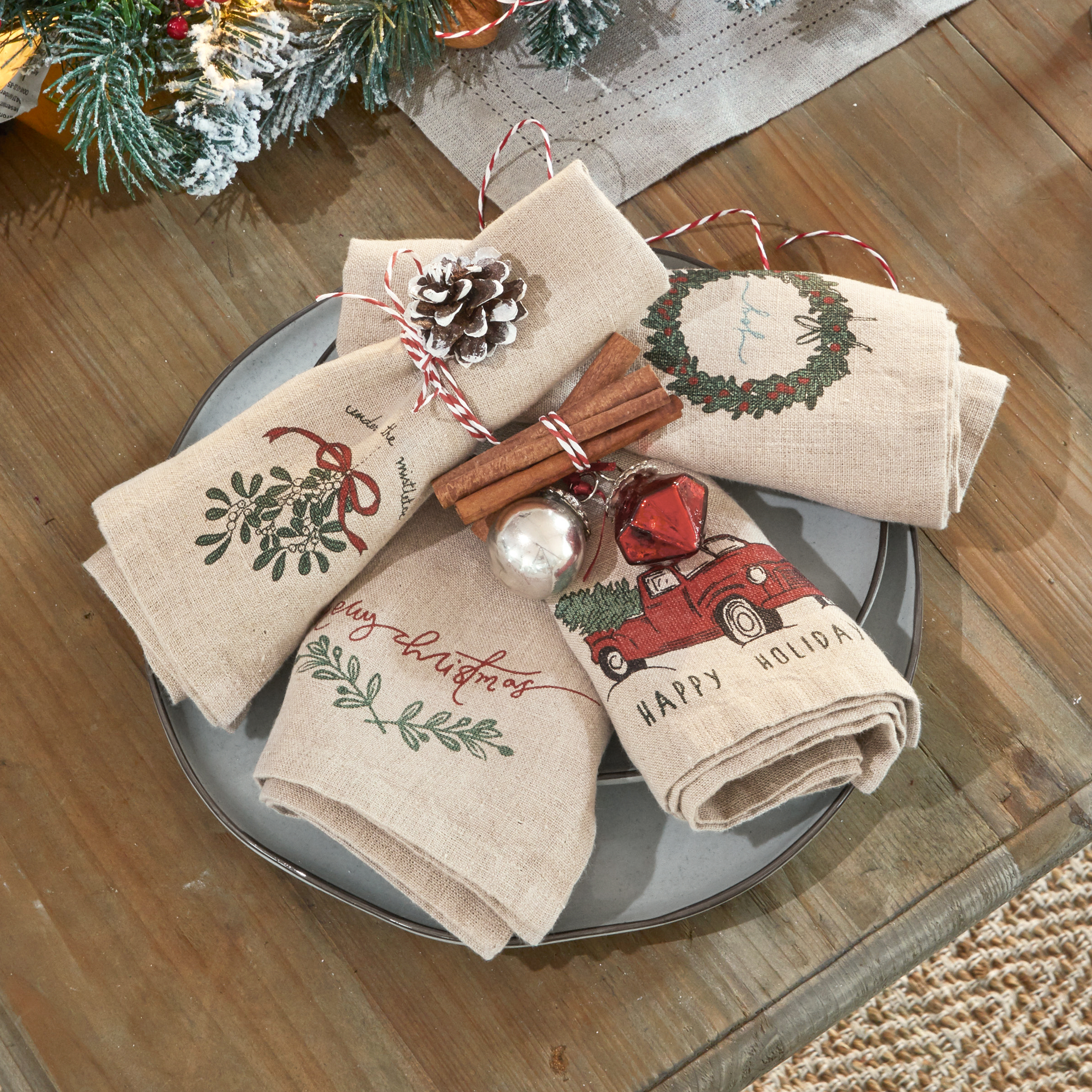 Servilletas de lino con motivos navideños, decoradas con ramas de canela y piña sobre plato gris