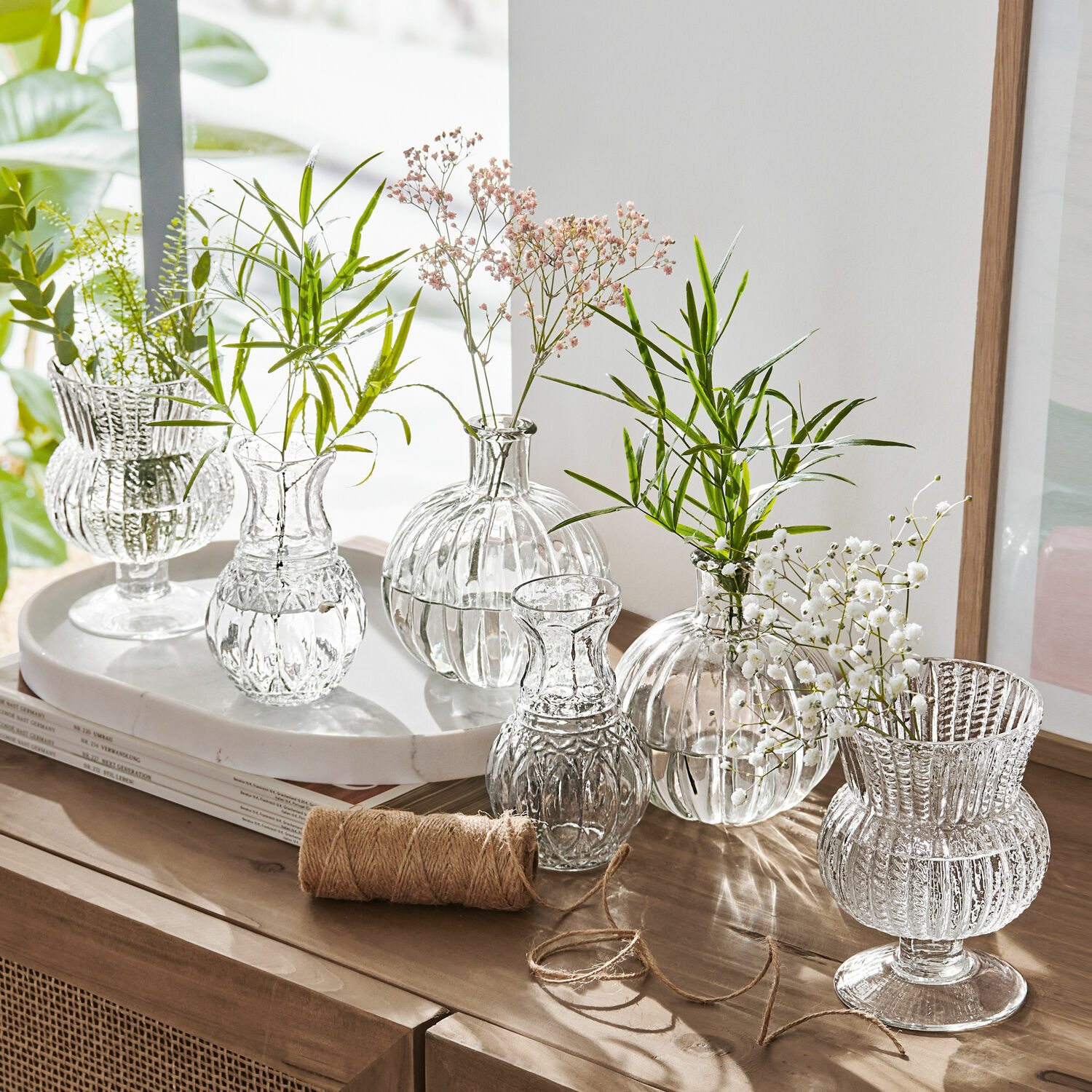 Set de 6 jarrones Amber Conjunto de jarrones de vidrio transparente con flores verdes y blancas sobre mueble de madera