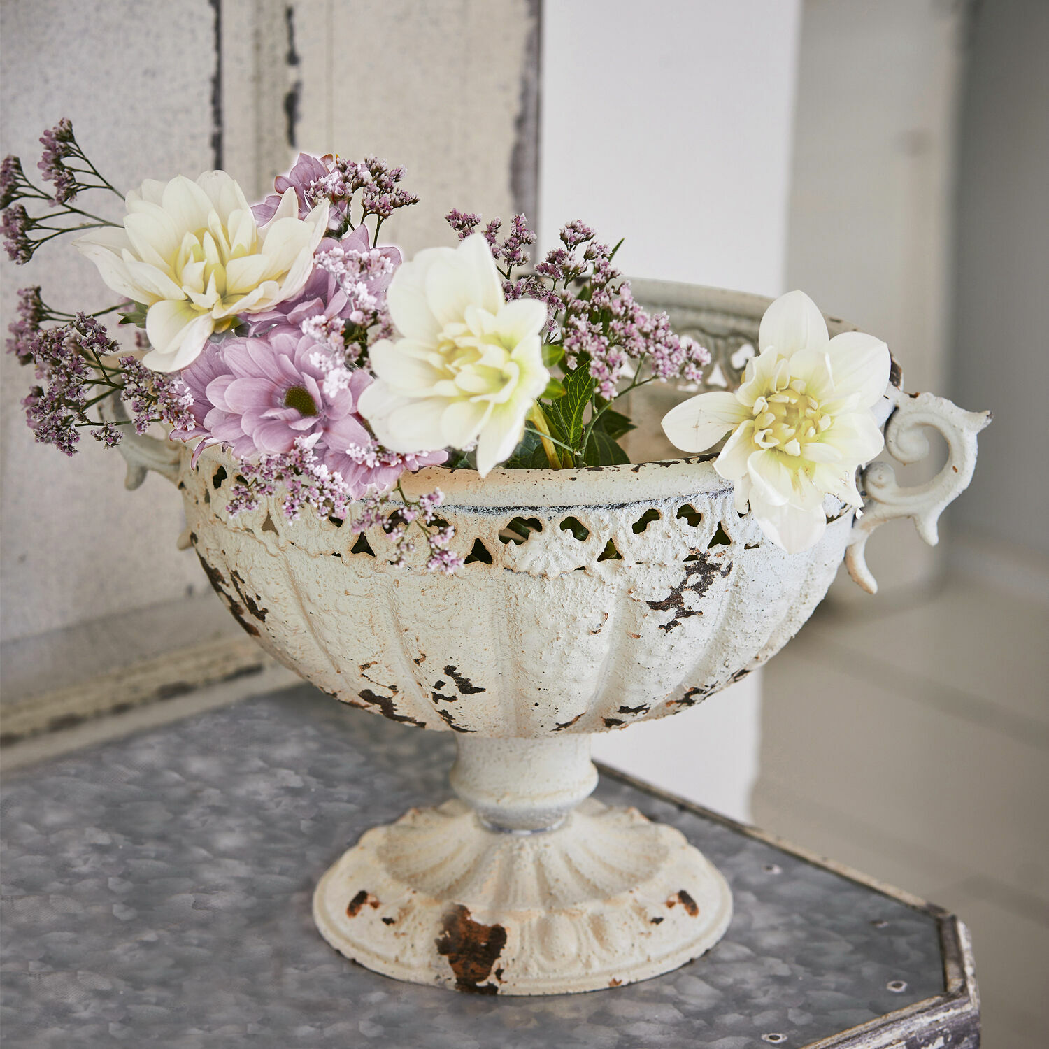 Ánfora Vescemont Cuenco metálico blanco envejecido con flores en tonos pastel sobre mesa decorativa interior