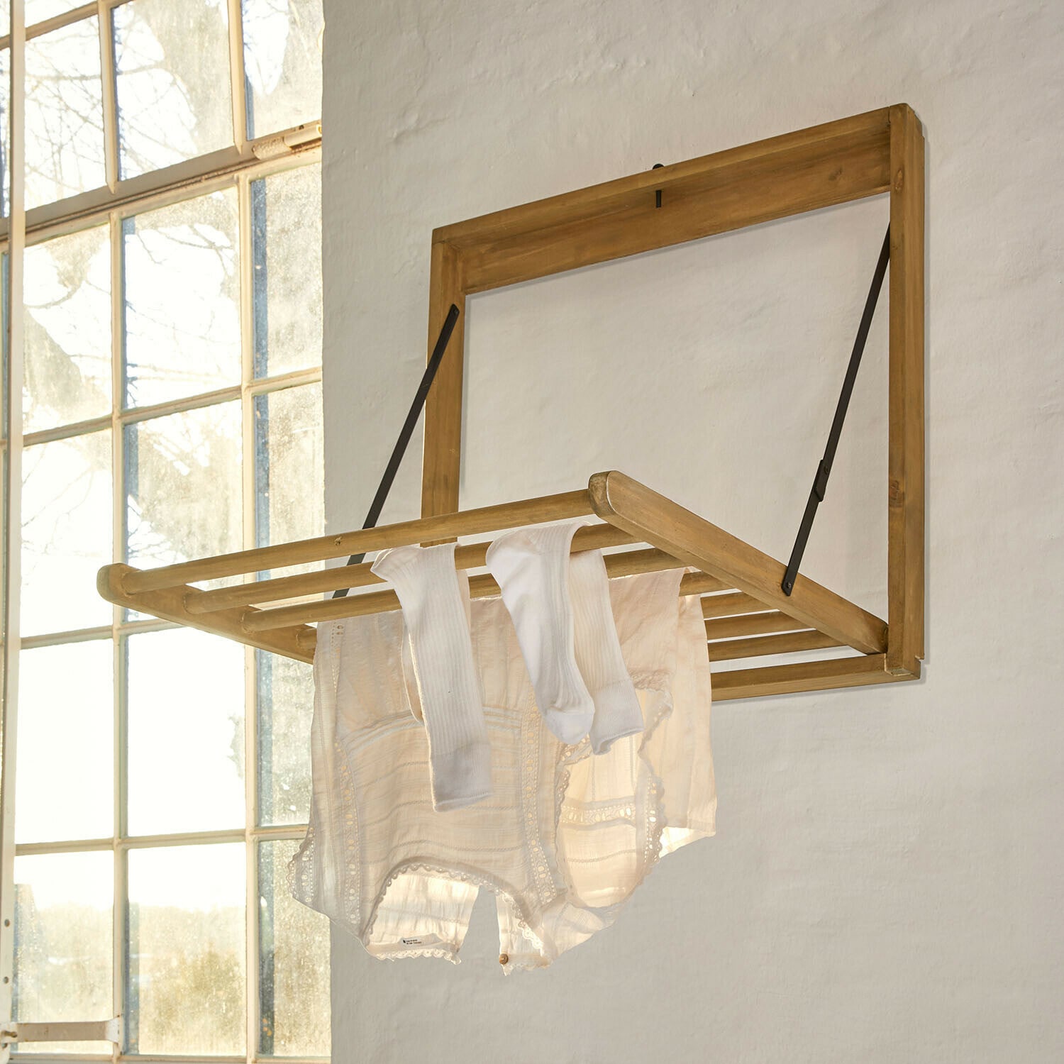Tendedero de pared Élirème Tendedero de pared plegable de madera clara con ropa blanca colgada en habitación luminosa