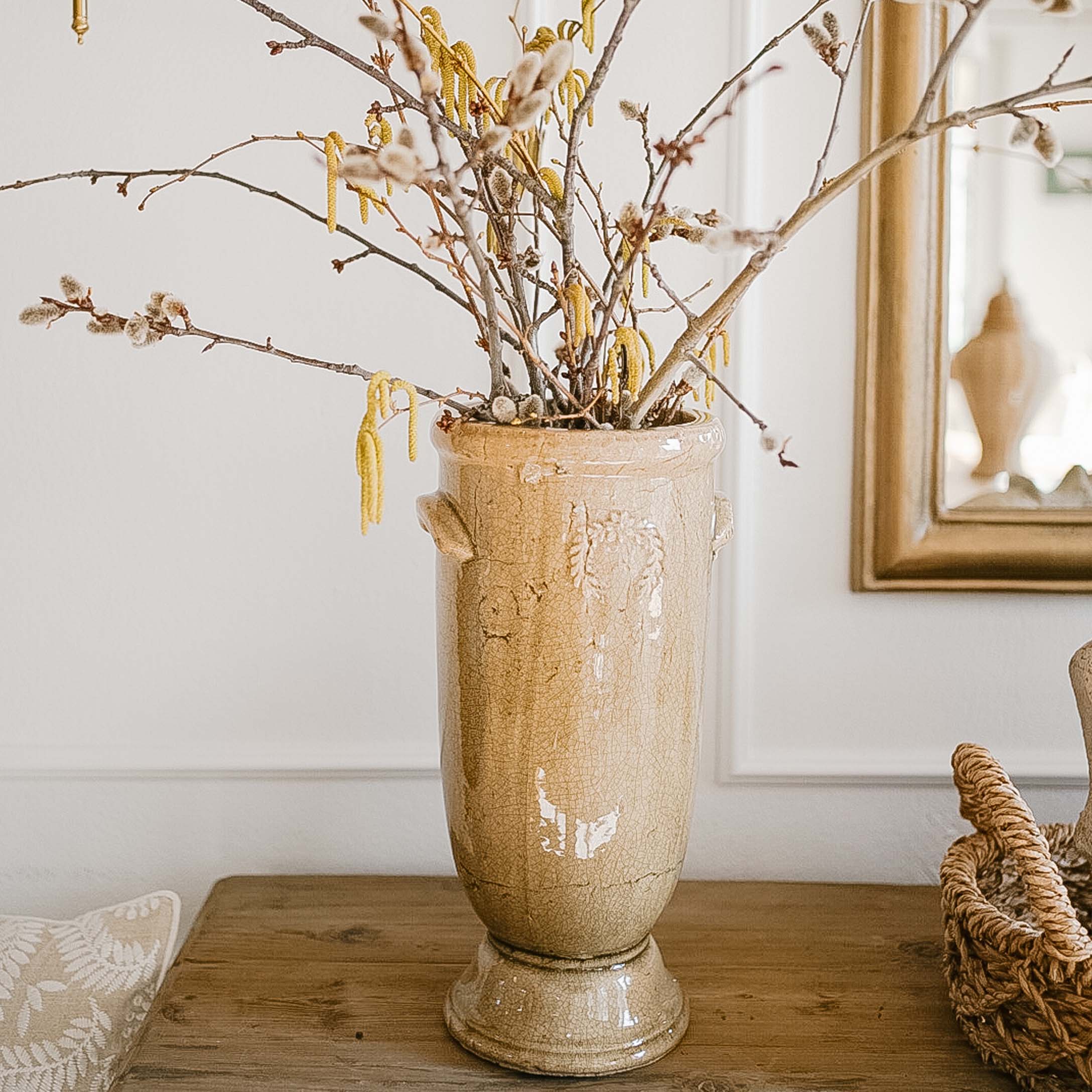 Jarrón de cerámica beige con flores y ramas sobre mesa de madera en interior luminoso