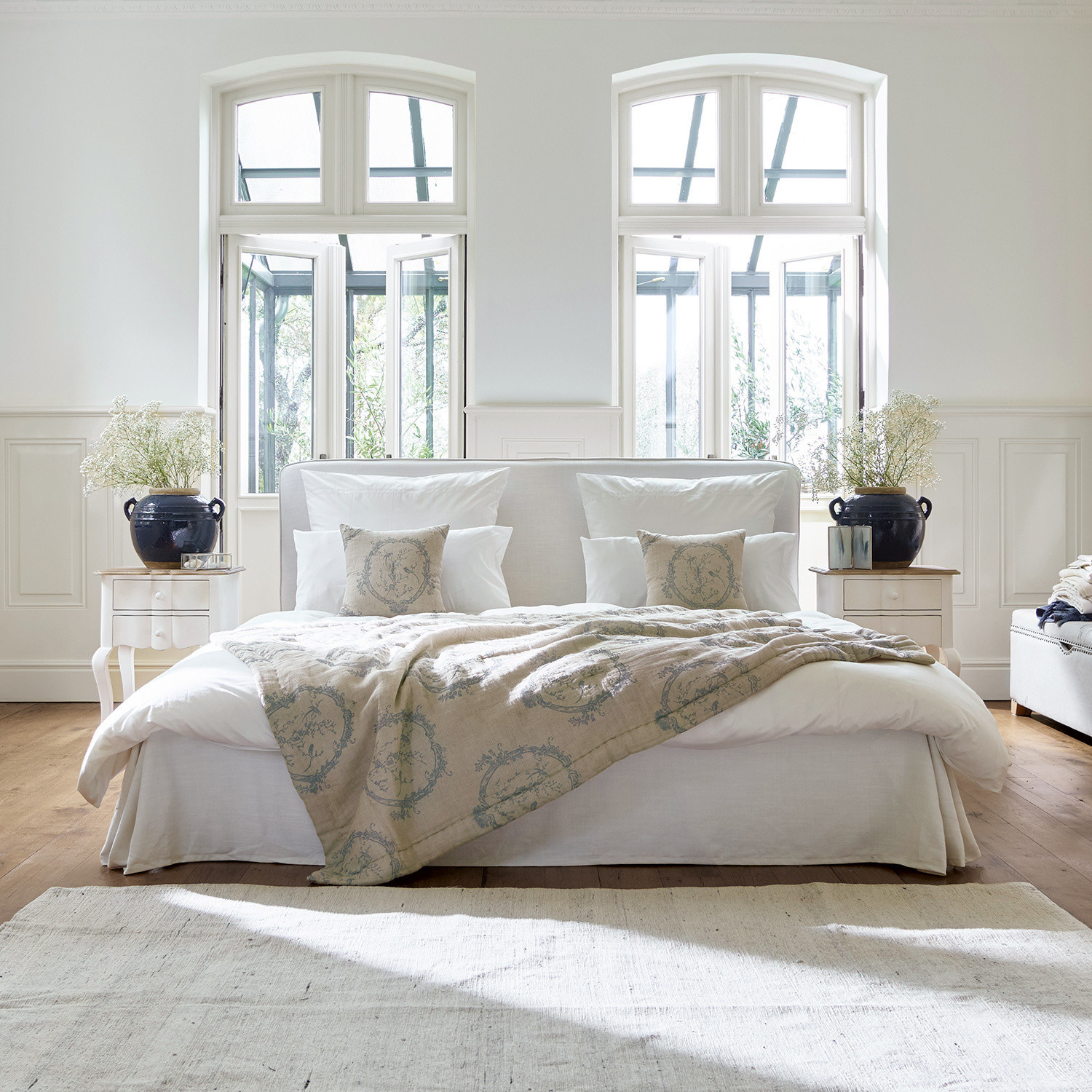 Cama Aubrianne Cama acogedora con tapizado claro y manta beige con diseño en dormitorio luminoso con grandes ventanas