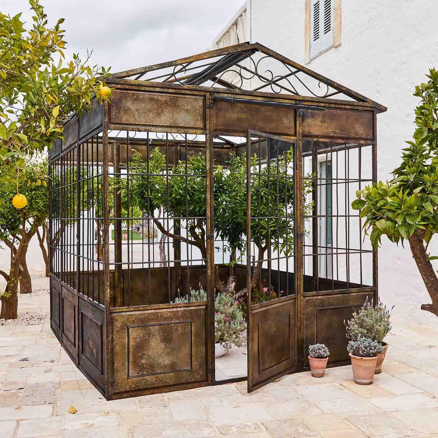 Pérgola de metal envejecido con plantas y árboles cítricos en terraza de piedra