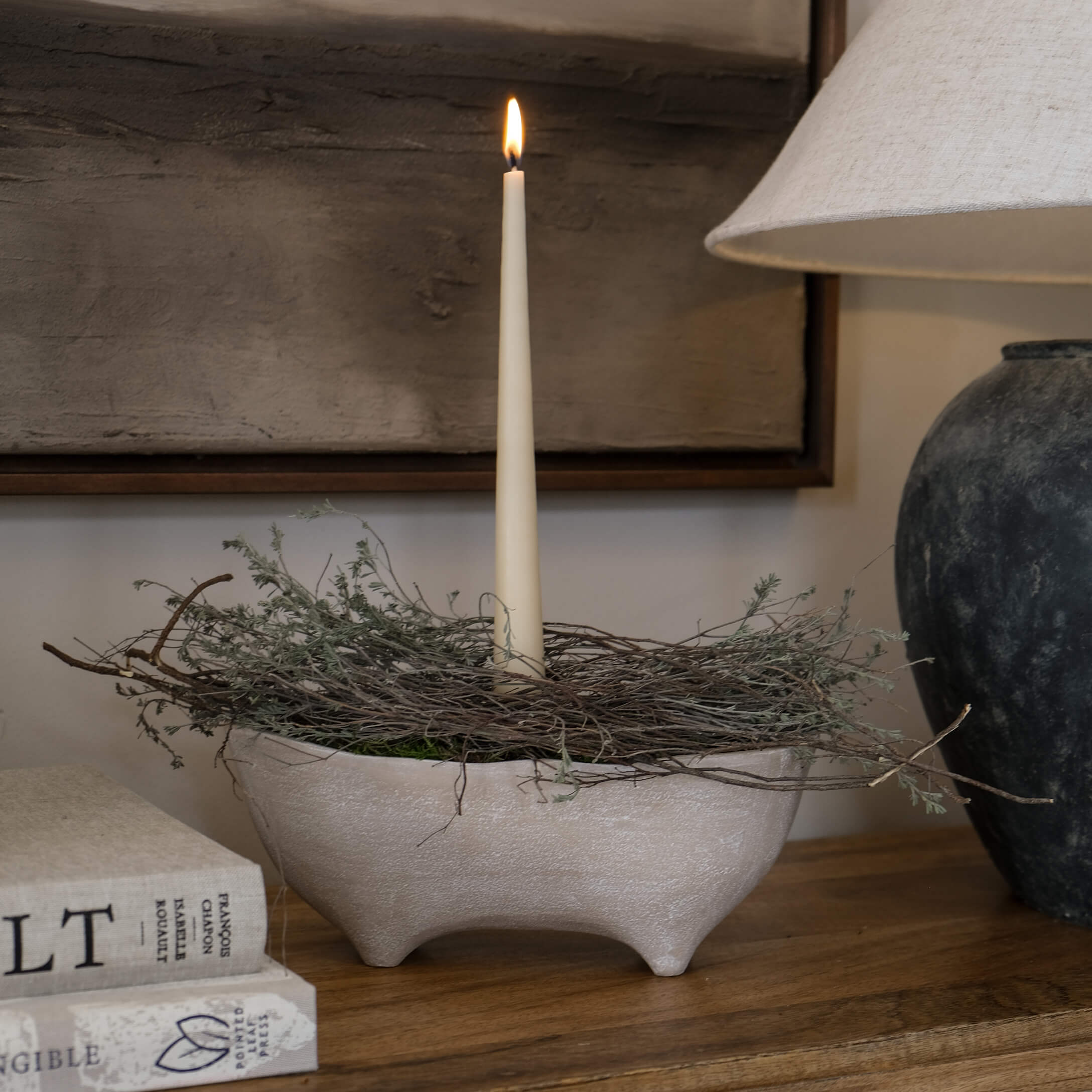 Cuenco de cerámica beige con tres patas, decoración de ramitas y vela blanca delgada
